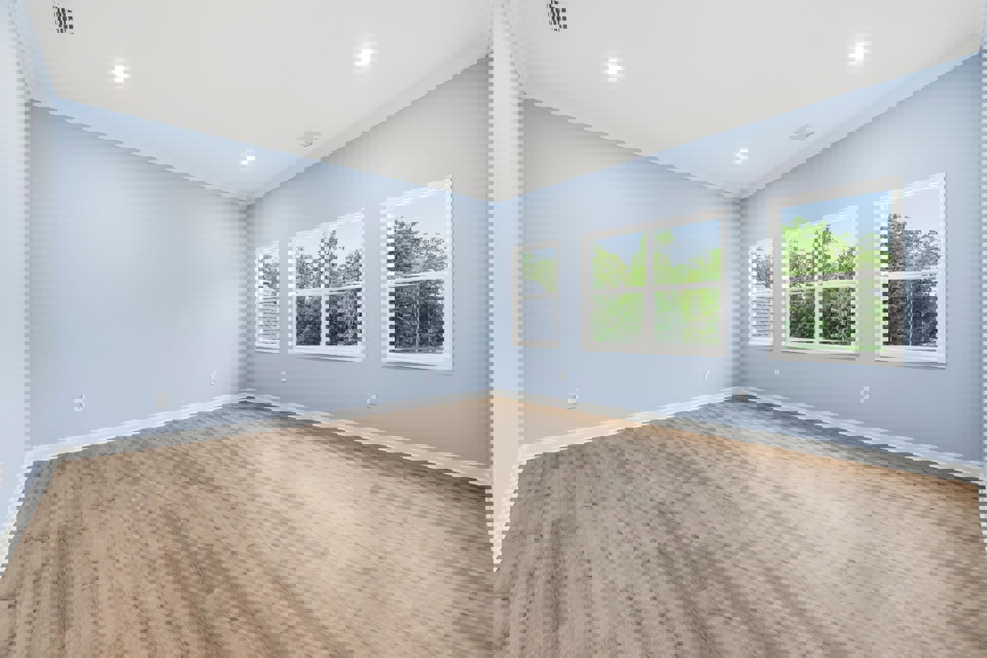 Blue-painted walls and hardwood flooring in a residential room, large window with view of trees and rooftops, white ceiling with recessed lighting