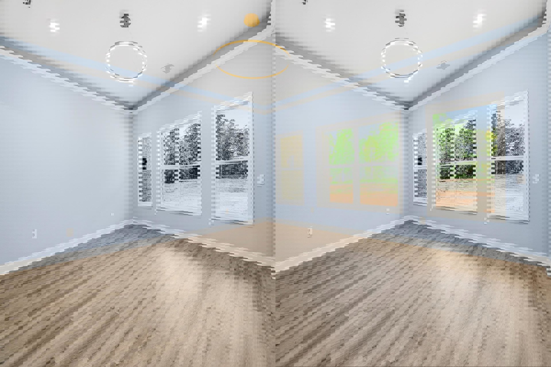 Wood plank flooring, large windows with tree views, circular ceiling light fixture, white walls and ceiling, modern interior design