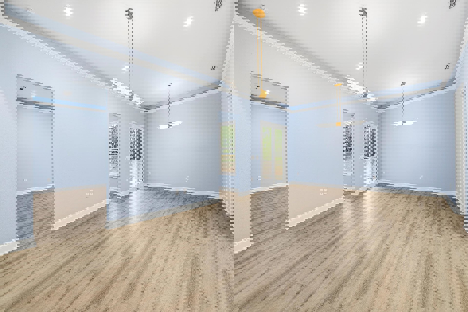 Wood flooring in a room with light blue plaster walls, ceiling light fixture, large window overlooking trees outside