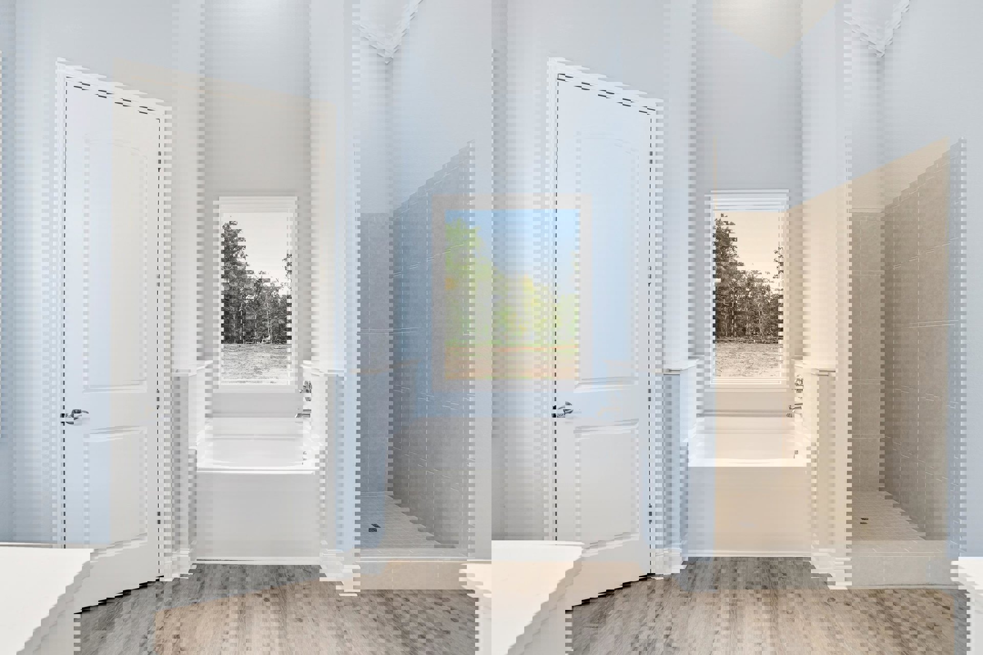 Bathroom with wood flooring, white bathtub, blue accent wall, window overlooking a field, white door with silver handle, and glass shower enclosure