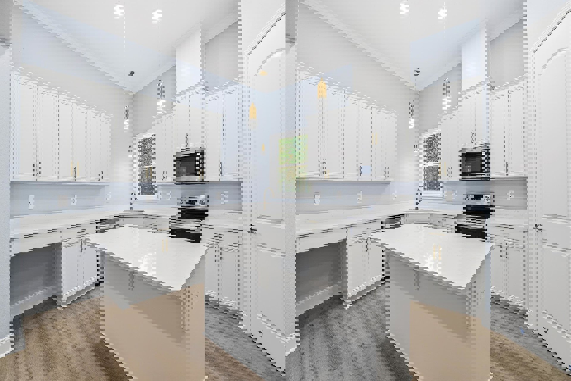 White kitchen with shaker cabinets, large white island, quartz countertops, stainless steel stove and microwave, window overlooking trees, light wood flooring, silver hardware on