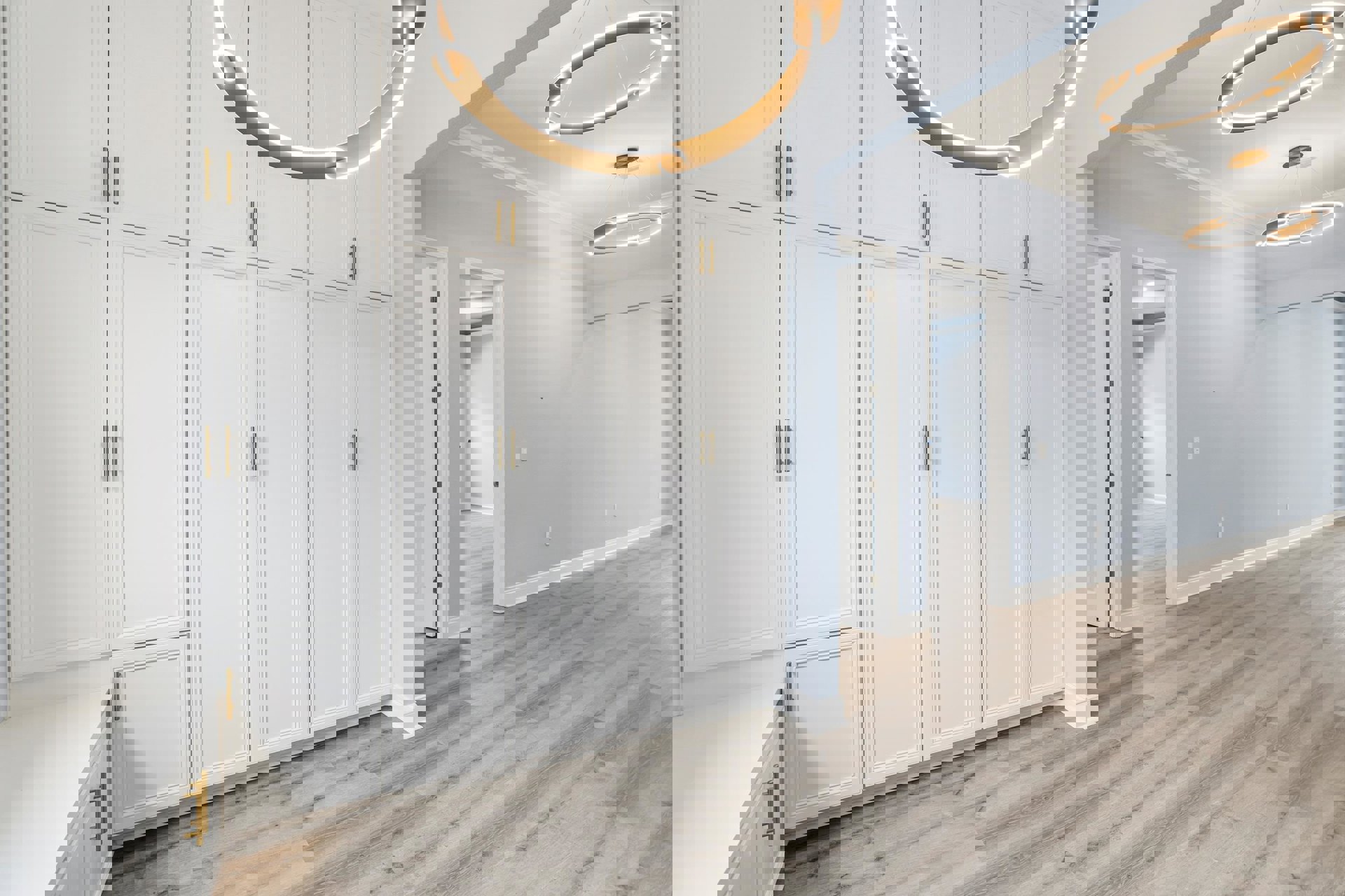 White cabinetry with gold handles, wood flooring, white countertop, and a white door with gold hardware; modern light fixture visible.