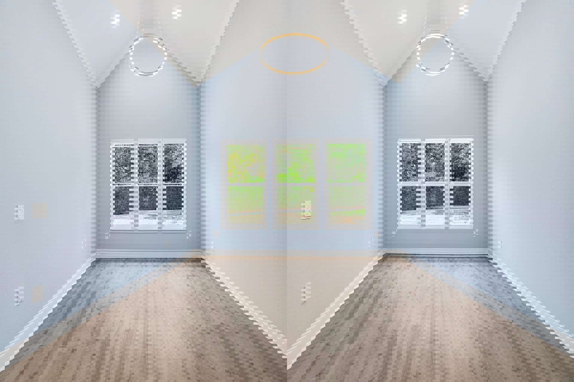 Wood flooring and blue accent wall in a bright room with large windows, circular white light fixture, and white light switch; trees visible outside.