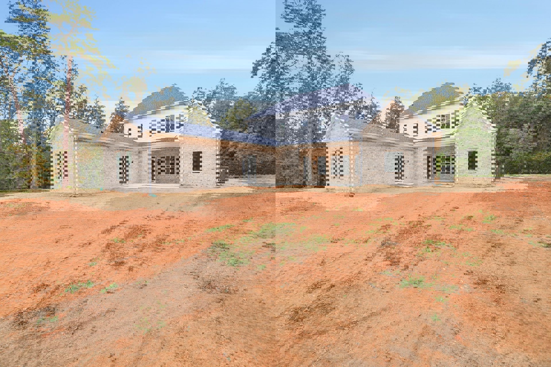 Two-story house with multiple windows, brick exterior walls, dirt yard area, and a tall tree with green leaves adjacent to the building