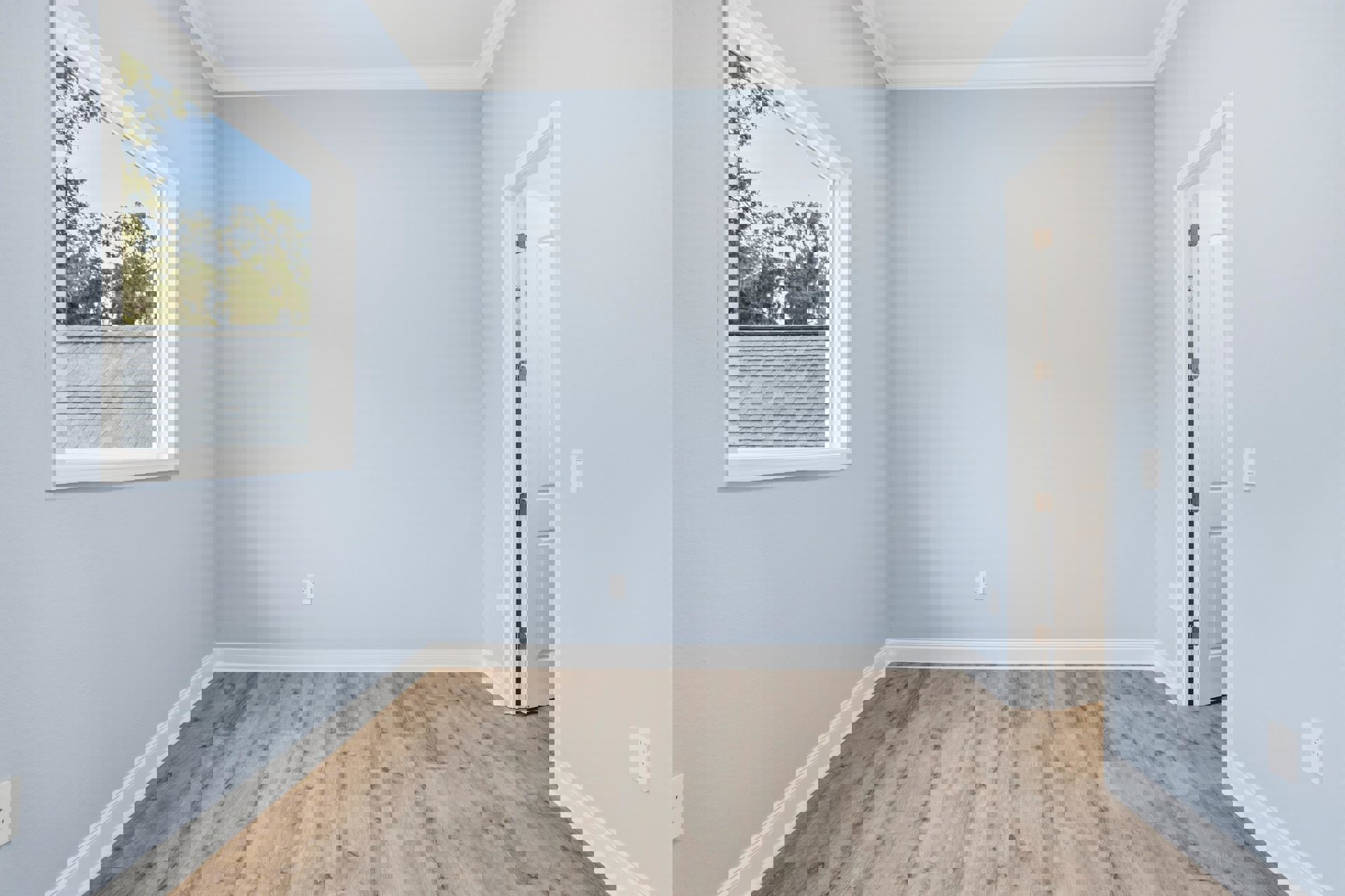 Wood flooring with white baseboards in a bright room featuring a large window overlooking trees and a roof, white walls, and ceiling.