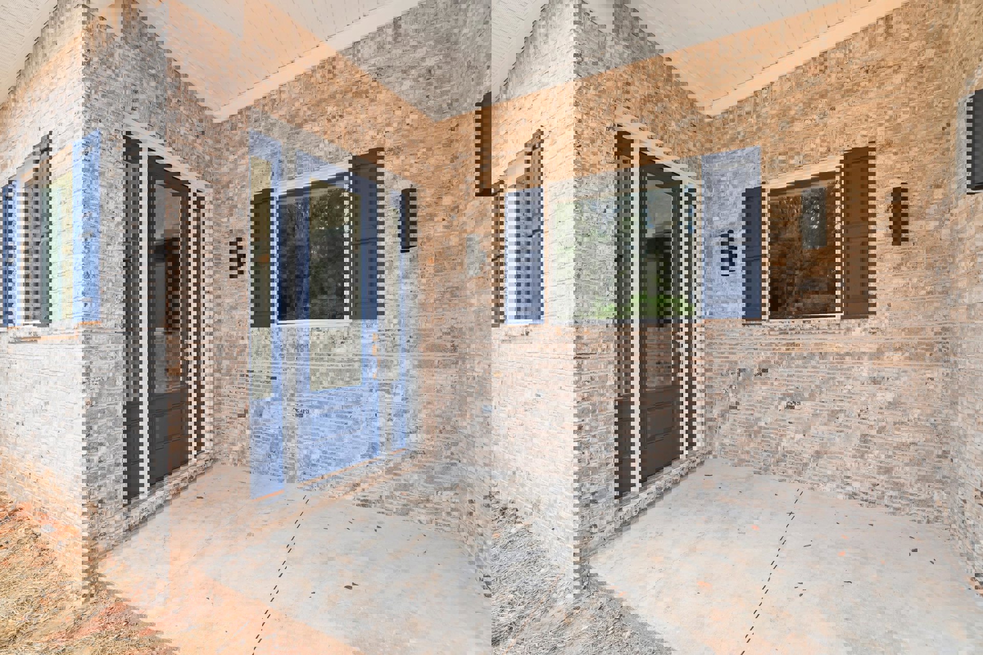 Red brick house with blue framed windows and a blue front door featuring a glass panel, surrounded by greenery and trees visible through the windows