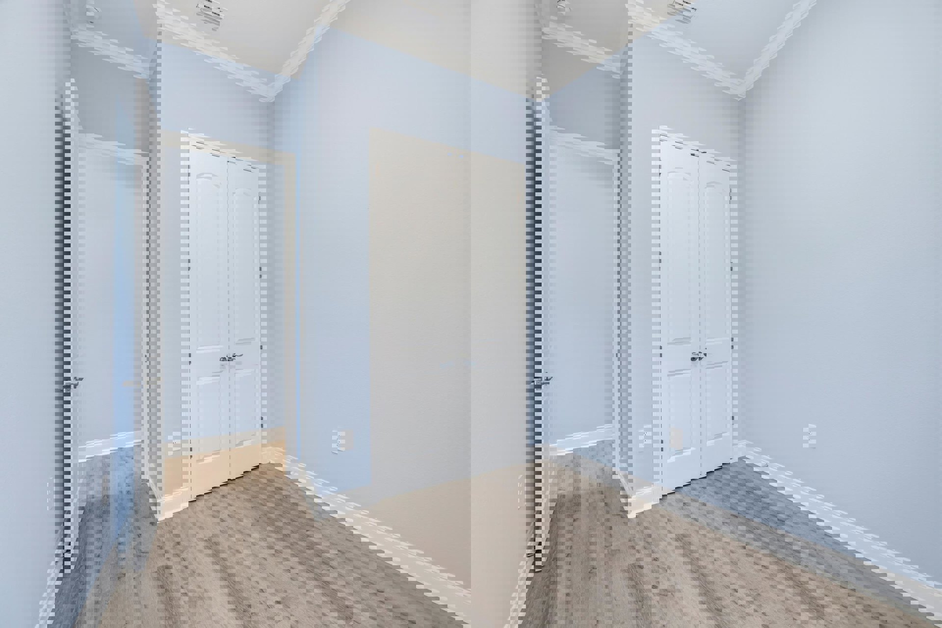 Room with wood laminate flooring, two white doors featuring silver handles, white walls, and simple molding.