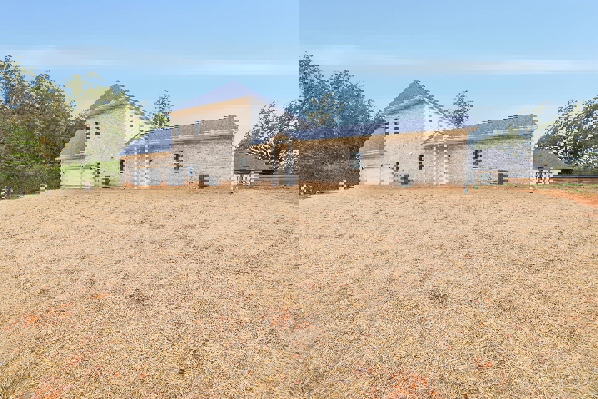 Brick house with white roof and garage, surrounded by grass field and trees, cloudy sky overhead