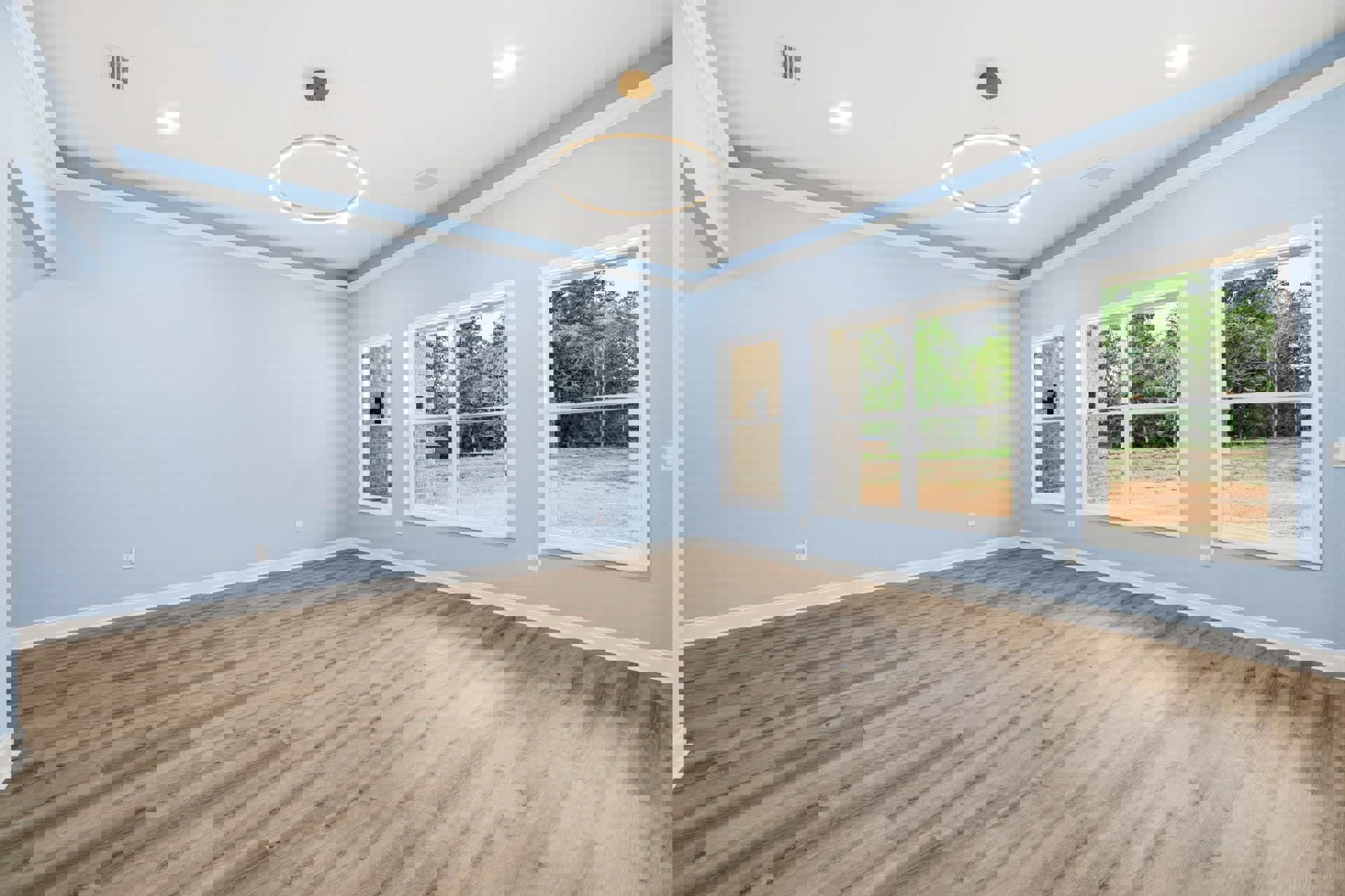 Wood floor room with blue walls, white trim, ceiling light fixture, and large windows overlooking trees.