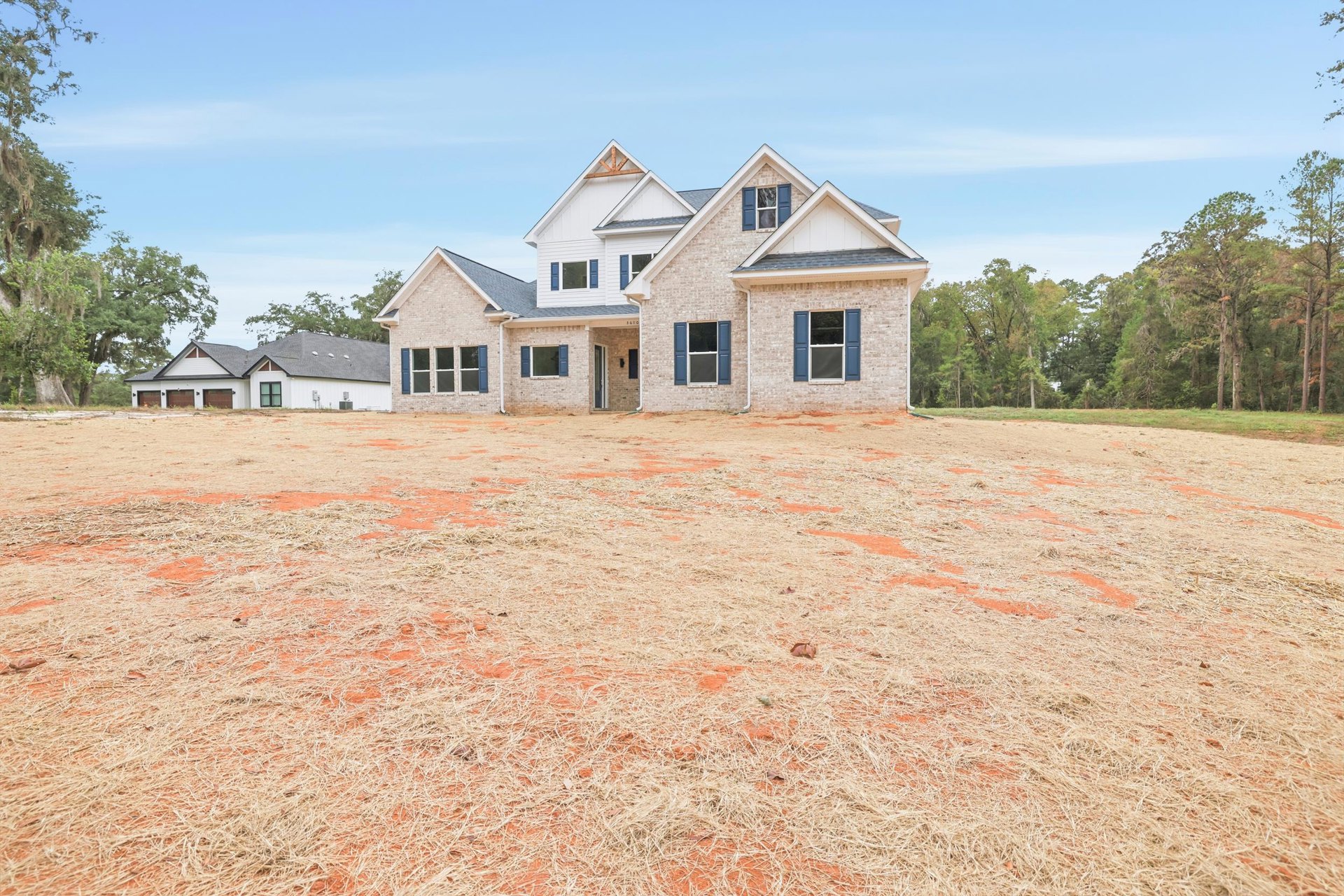 Two-story house with black roof, white-framed windows, blue shutters, surrounded by a large grassy field under a partly cloudy sky