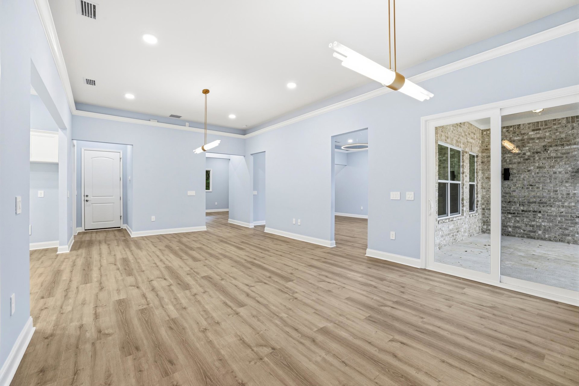 Wood flooring with white walls and columns, white door with silver handle, ceiling light fixture, blue accent wall in background
