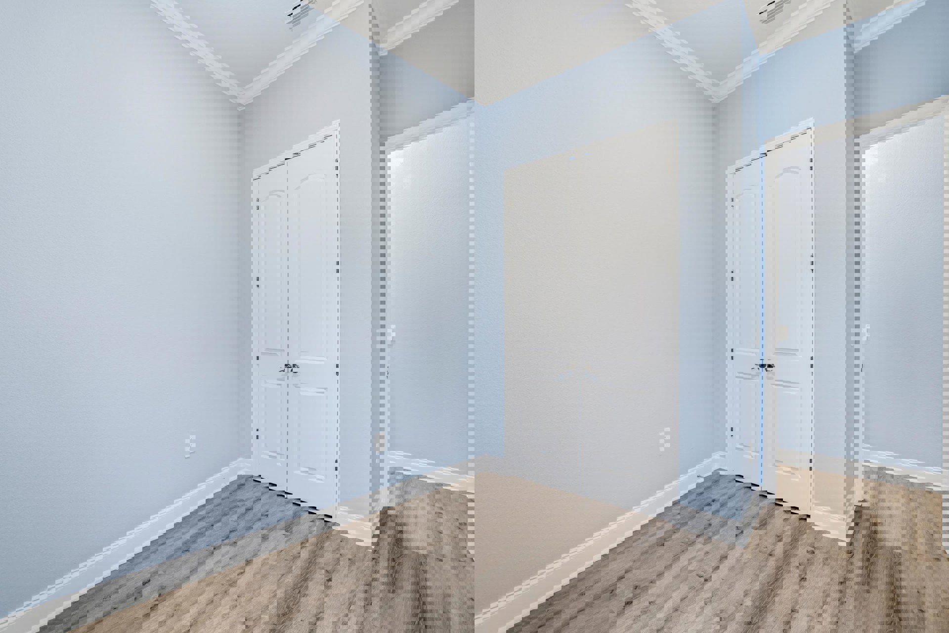 Wood floor with white baseboards, two white doors, light switch beside one door, white ceiling molding, plaster walls