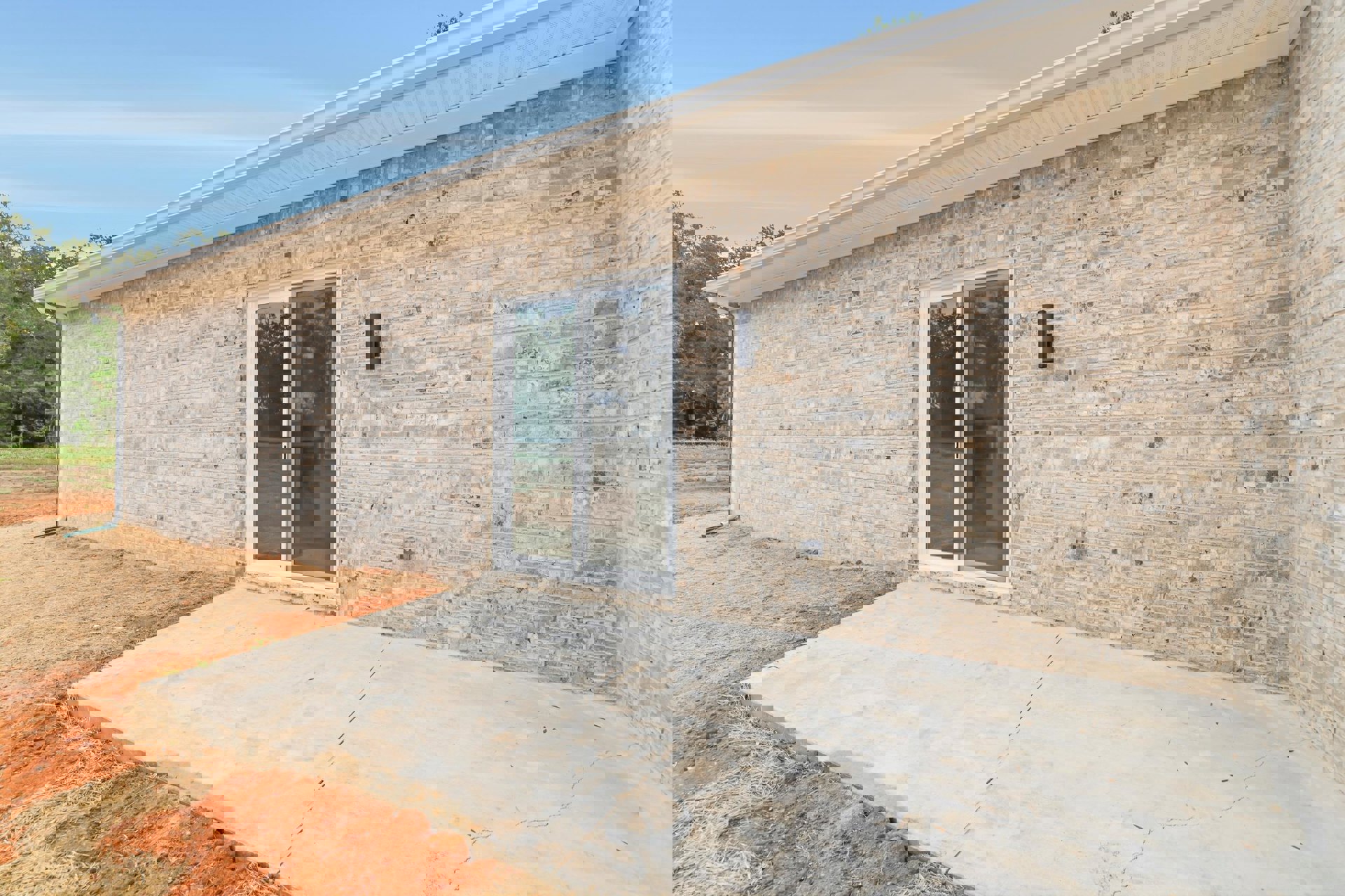 Red brick exterior with a sliding glass door, white-framed window, and concrete patio surrounded by trees