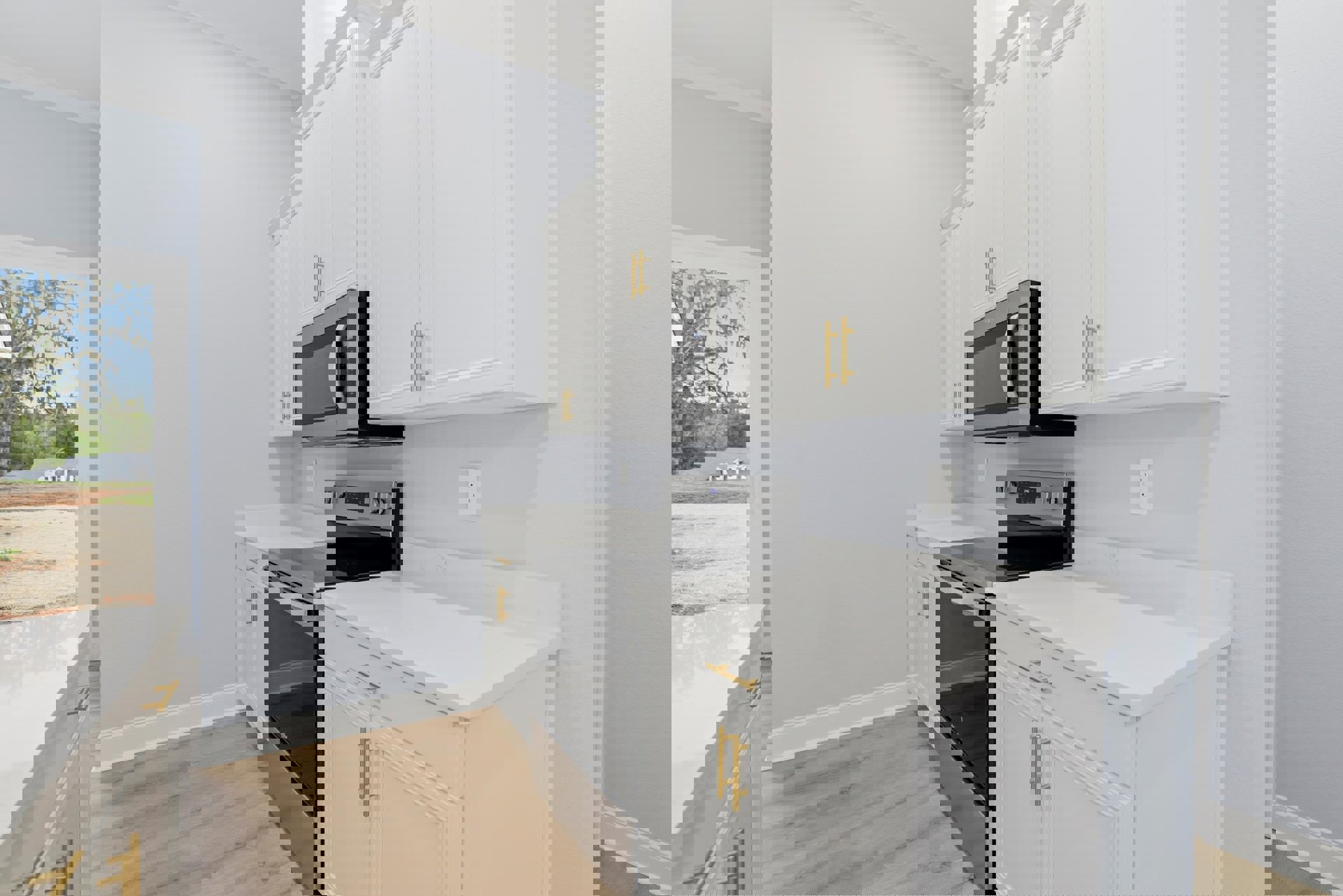 White kitchen with shaker cabinets, gold hardware, black microwave, white countertop, stainless stove, window showing tree and blue sky, black refrigerator in foreground.