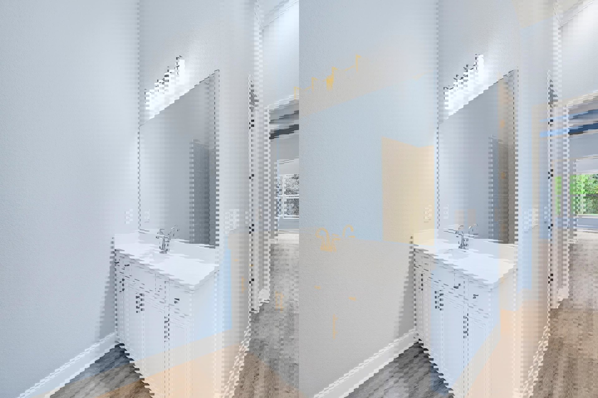 White bathroom with gold-handled faucet, rectangular mirror above sink, white tile wall, window showing green trees, and white door with matching frame