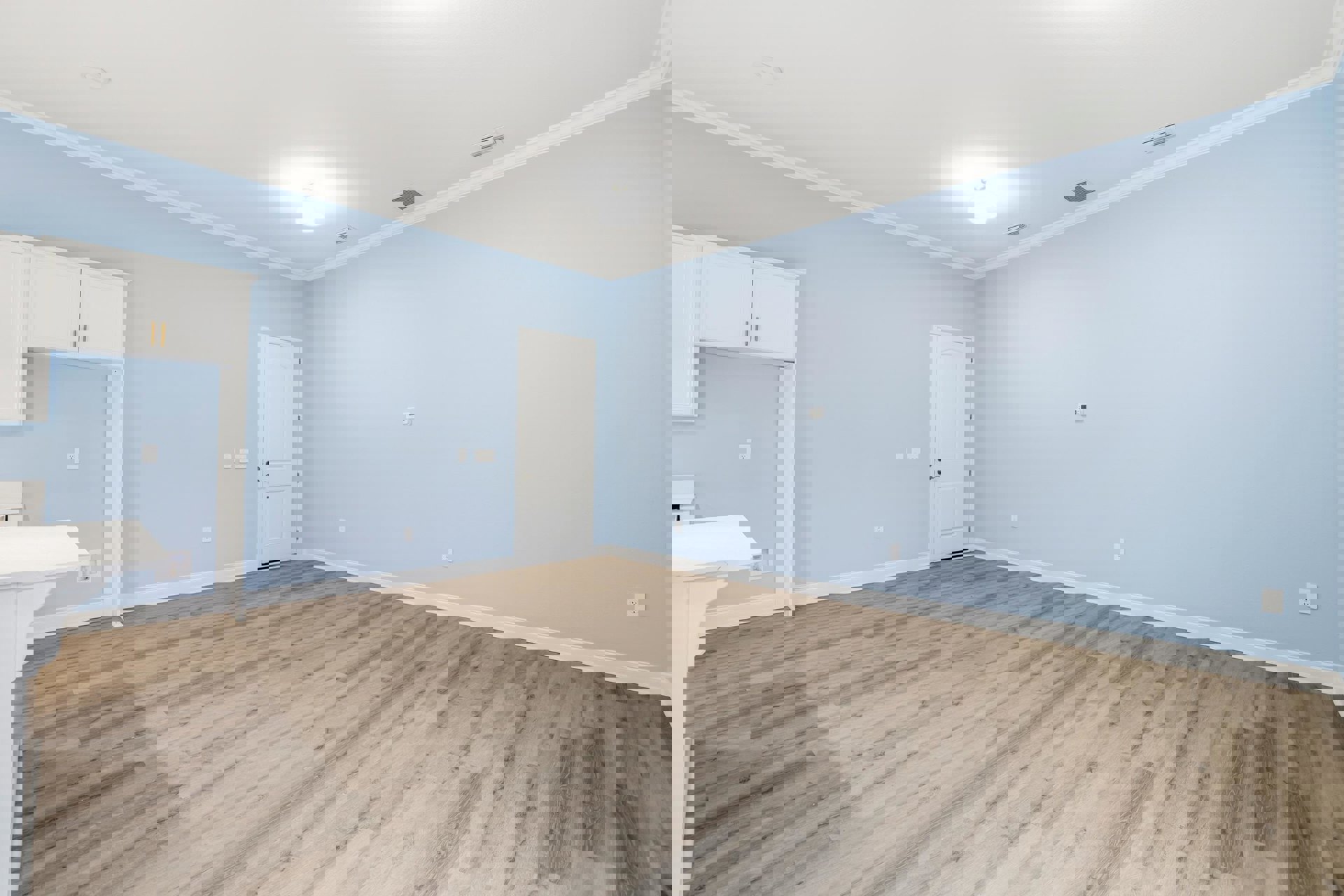 Room with light wood flooring, white walls, white ceiling with recessed light fixture, white door with silver handle, and white cabinet featuring gold handles.