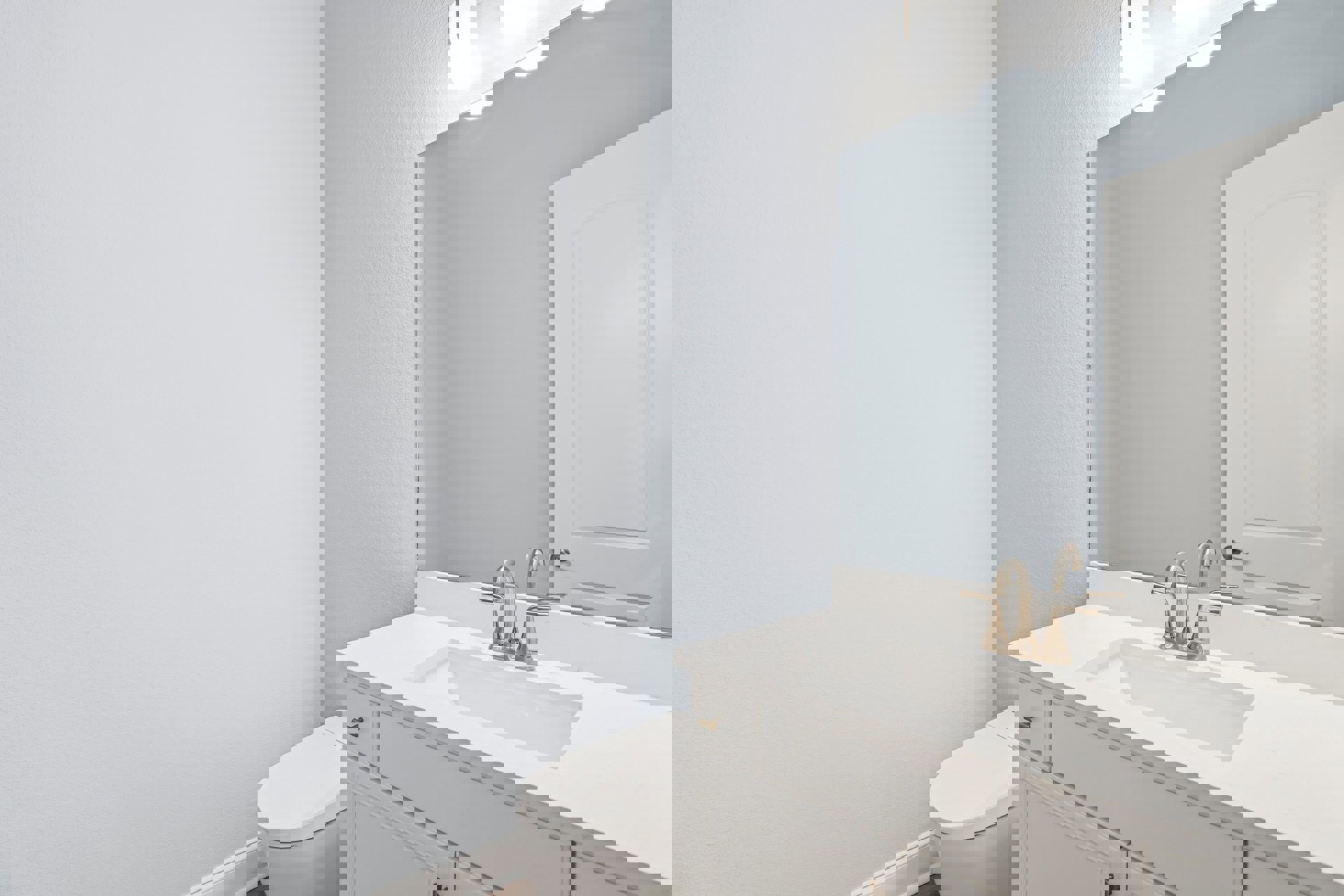 Modern bathroom with white tile walls, rectangular mirror above a sleek sink and chrome faucet, white toilet, decorative framed door, and minimalist fixtures