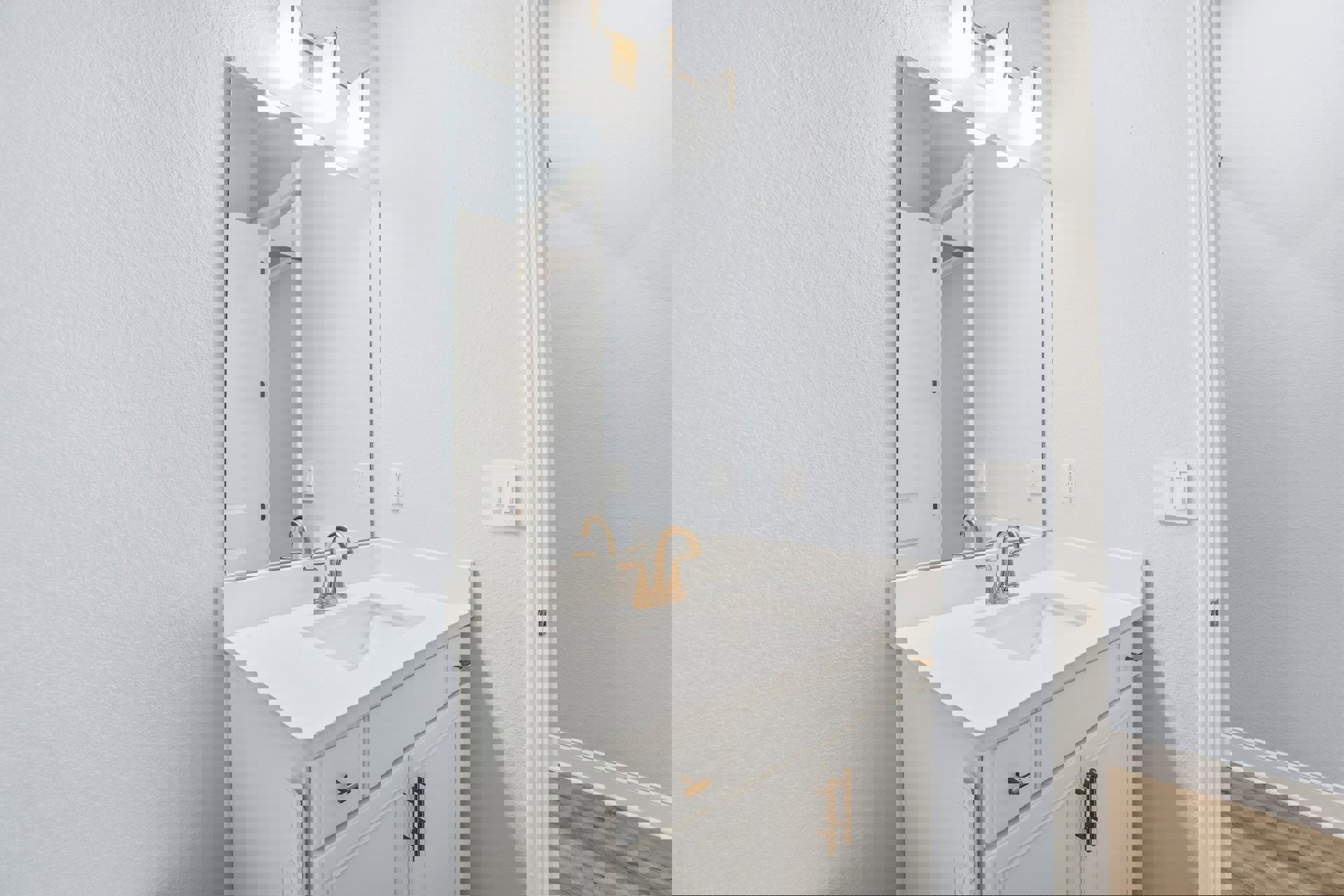 Bathroom with wood flooring, white baseboard, rectangular mirror above a white sink, three-light fixture, and white wall switch