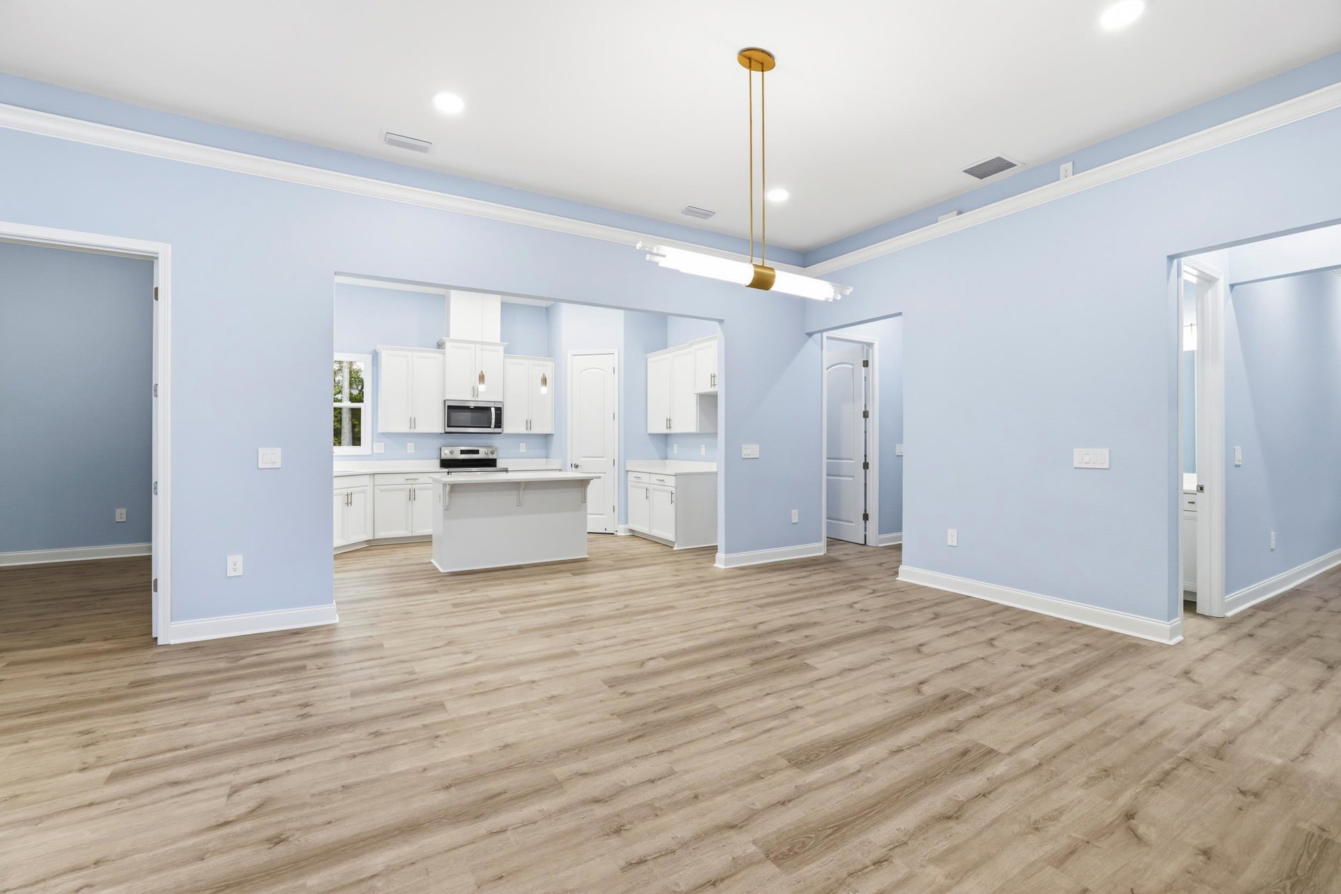 Wood flooring with white cabinets, white walls, gold poles, white door with metal handle, white countertop with yellow handle, ceiling light fixture