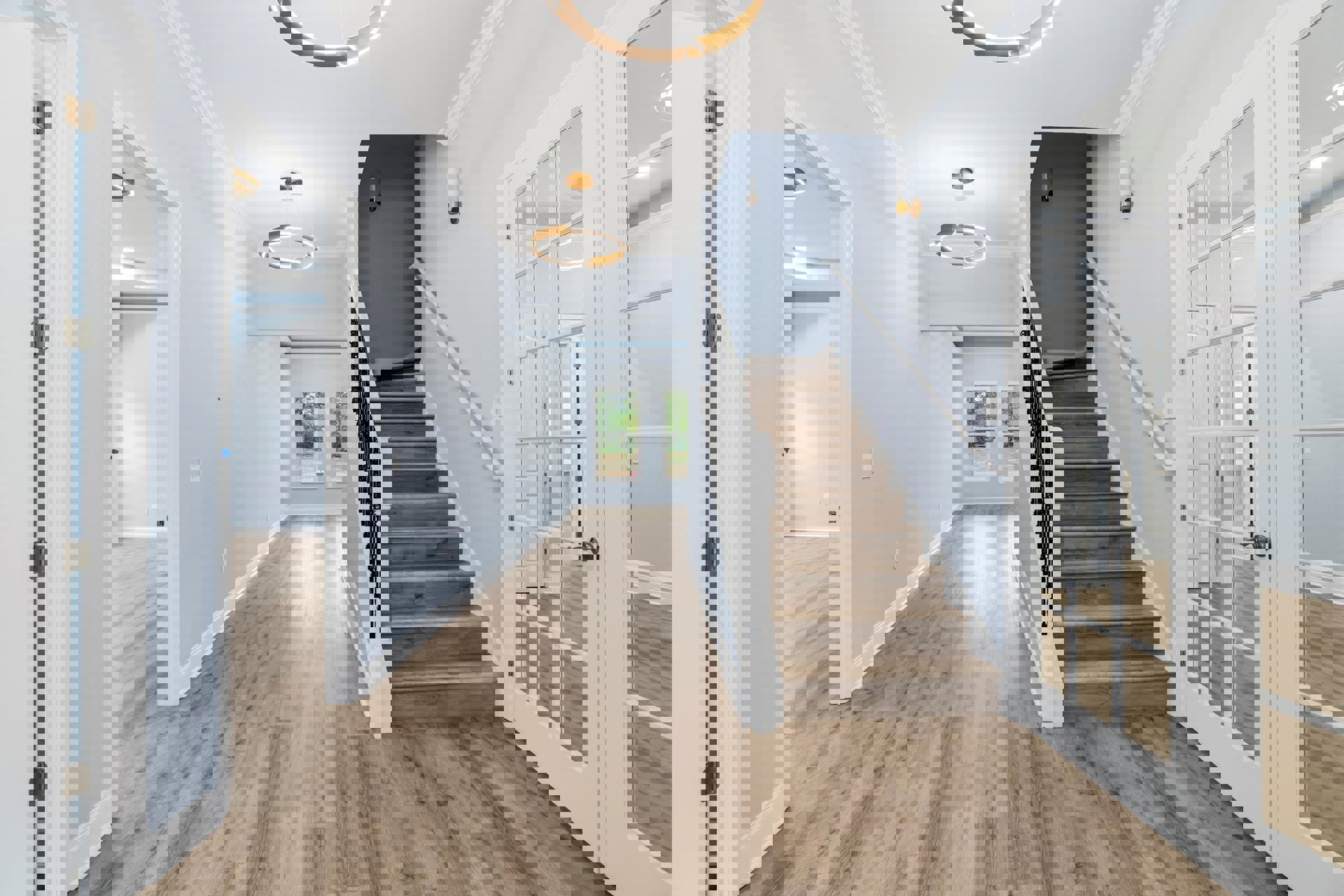 Hallway featuring warm wood flooring, wood staircase with matching railing, white walls with crown molding, ceiling light fixture, and a window overlooking trees.