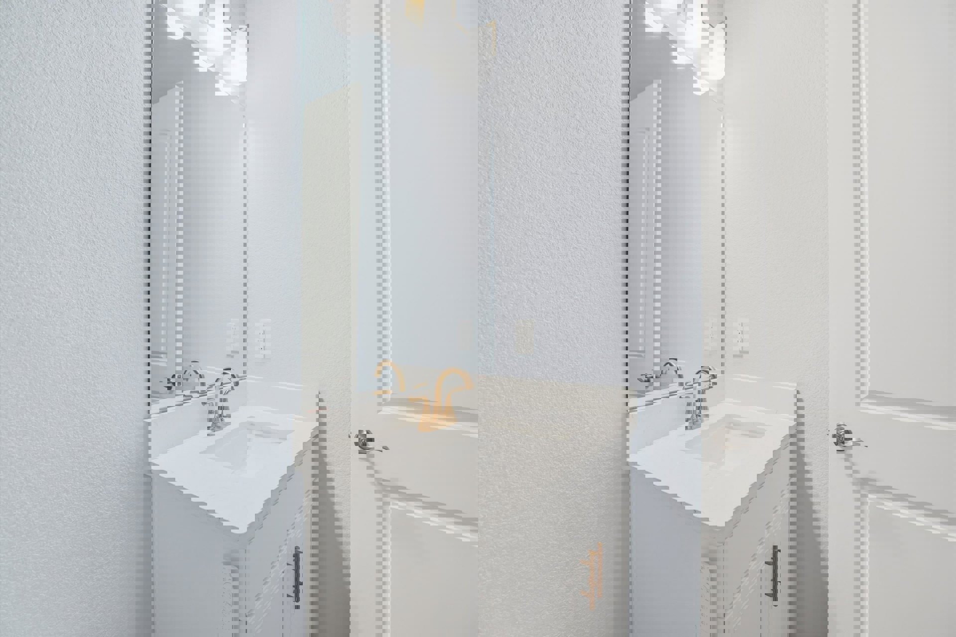 White bathroom with rectangular mirror above a modern sink, chrome faucet, tiled wall, and white cabinetry