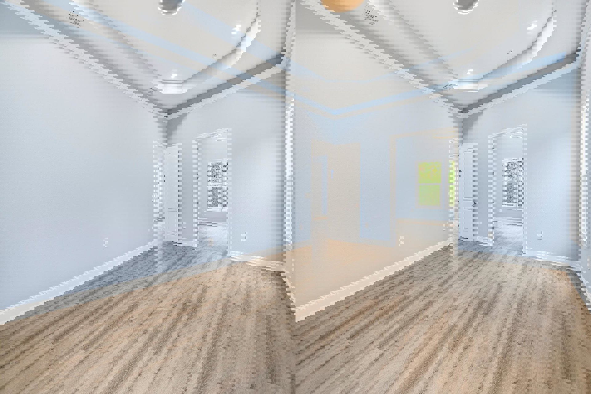 Wood flooring and light blue plaster wall, white door with blue ribbon, ceiling light fixture, window showing trees outside