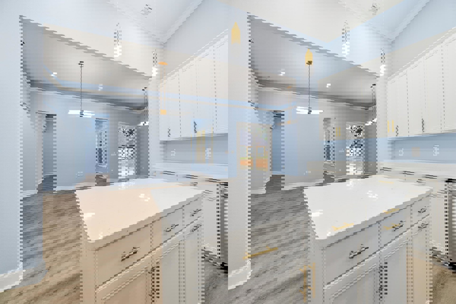 White kitchen with gold hardware, wood flooring, light blue walls, white island, window overlooking neighboring house, integrated sink and tile backsplash.