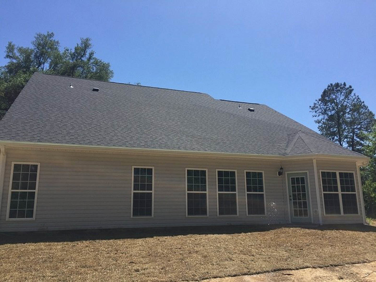 Two-story house with white siding, multiple square-paned windows, manicured green lawn, and mature trees in the background