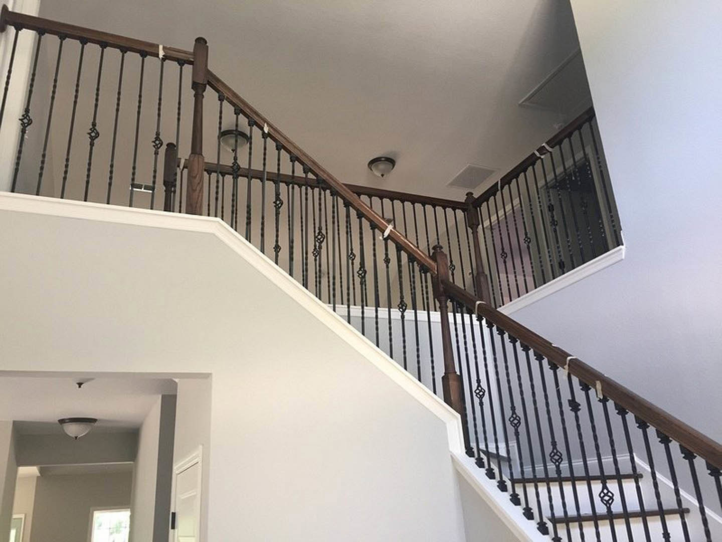 Open staircase with black metal railings, light fixture on ceiling above, white walls, and sunlight streaming through nearby window