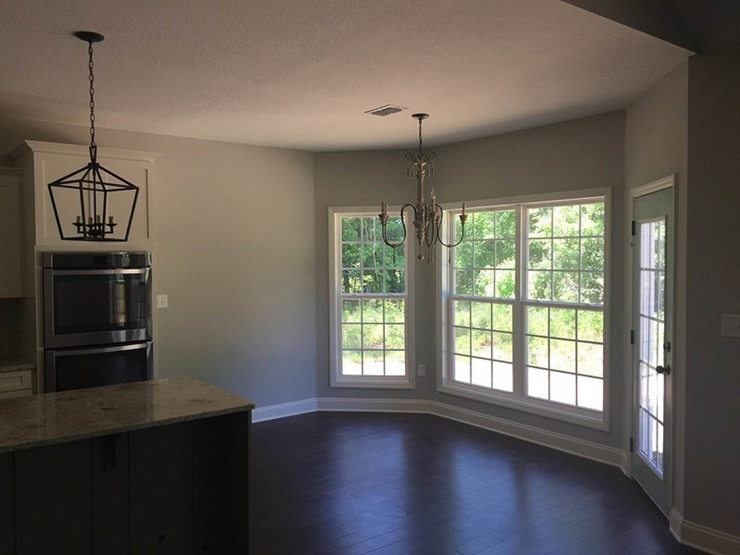 Kitchen with dark hardwood floors, white molding, multi-pane windows, white cabinetry, double oven, and ornate chandelier hanging from the ceiling
