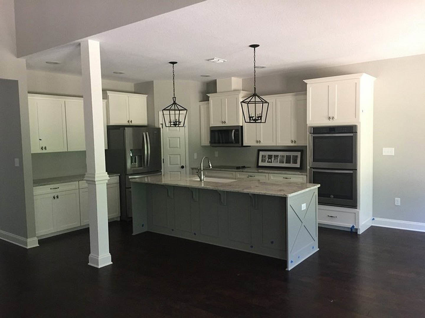 White cabinetry kitchen featuring a spacious central island with white countertop, stainless steel refrigerator, built-in microwave, undermount sink, and light wood flooring.