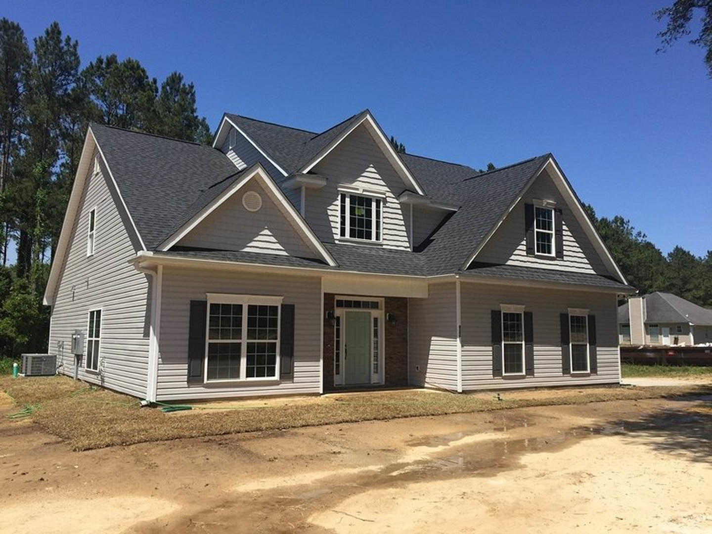 Two-story home with white siding, green front door, white-trimmed windows, covered porch, paved driveway, and patch of bare dirt in front yard.