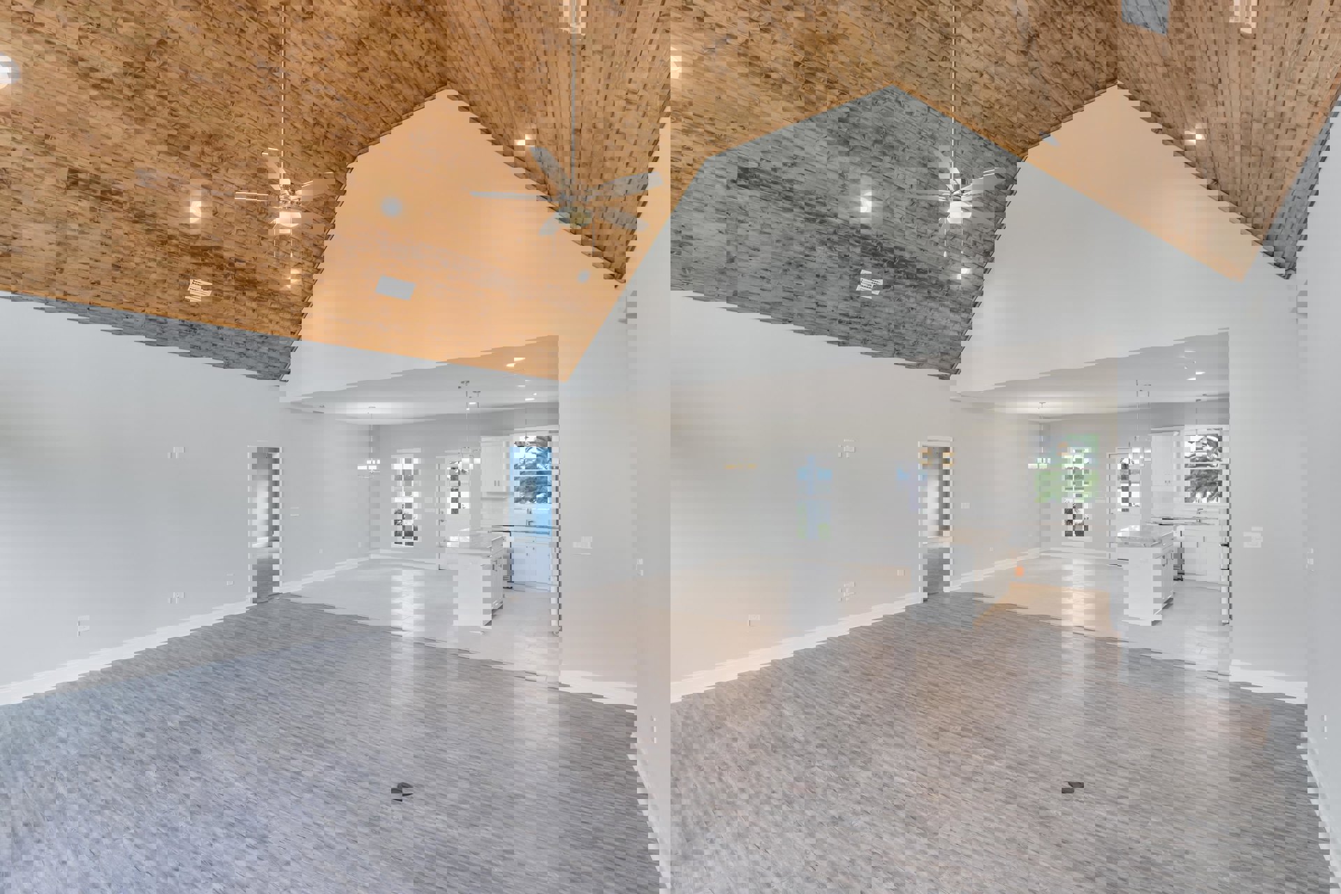 Open-concept living area with wood flooring, ceiling fan with light, white kitchen featuring marble island, blue accent wall, white door, and large window providing natural light.