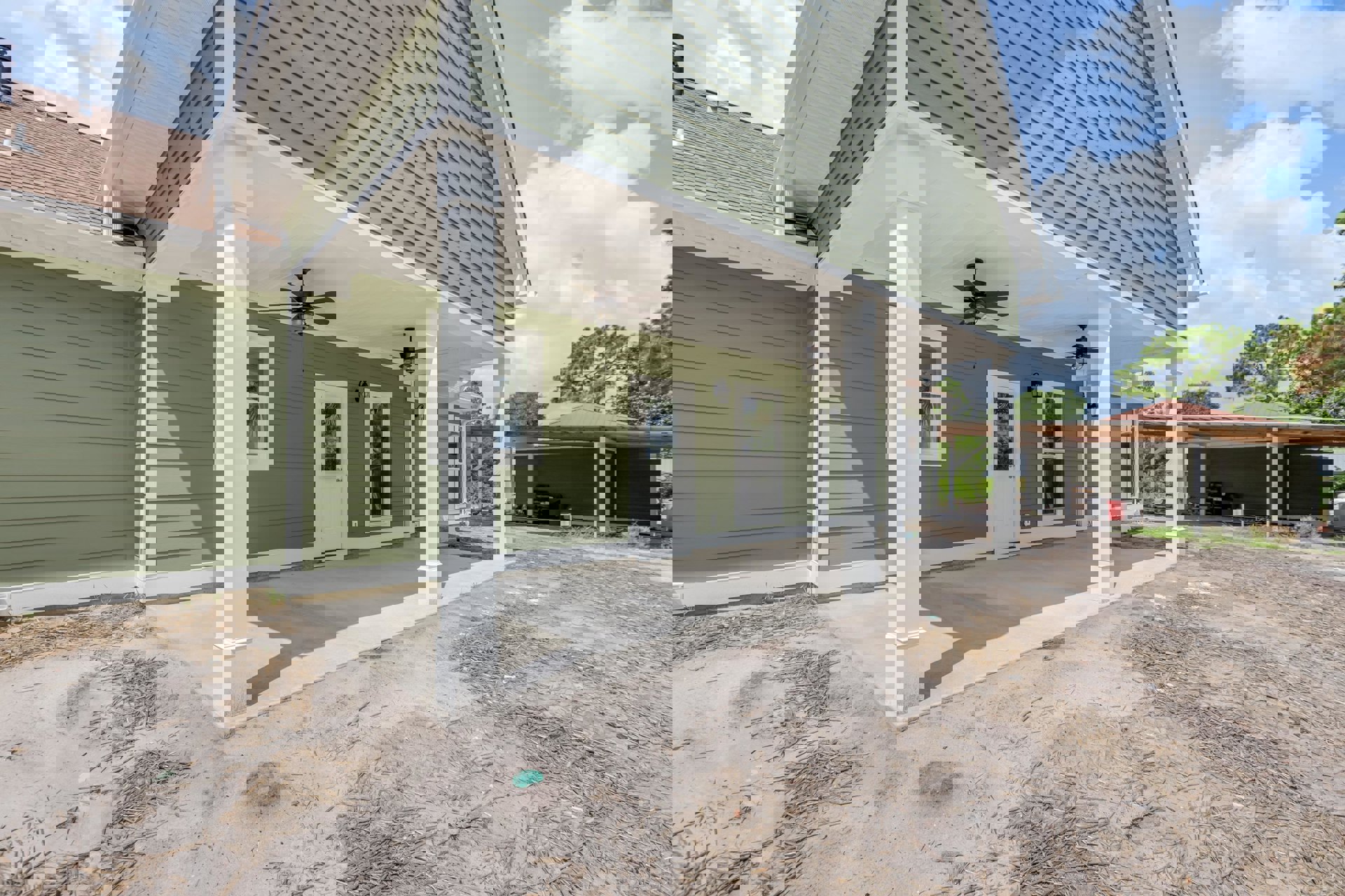 Green exterior walls with white columns and trim, covered porch featuring a ceiling fan with light, white framed windows, and a white door with glass inset