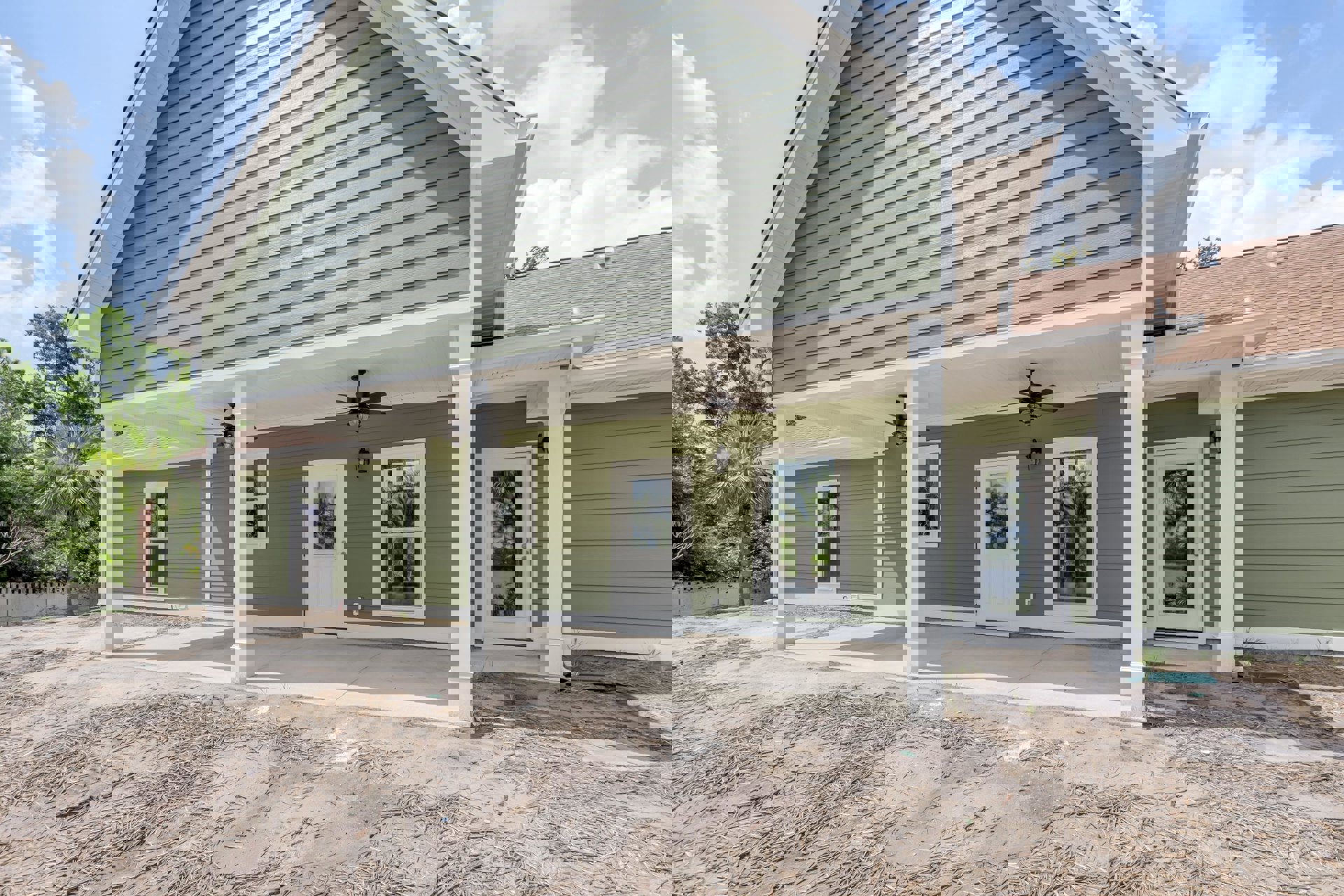 Green exterior siding with white trim, white-framed window, white door with glass insert, white pillars supporting porch roof, cloudy sky overhead