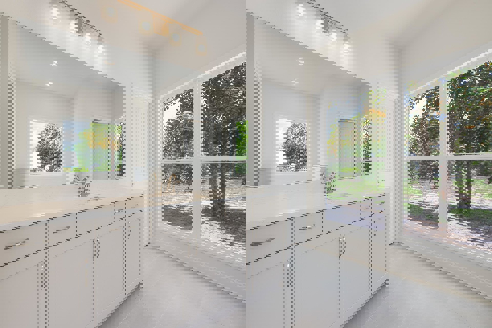 White bathroom featuring a wide vanity mirror, expansive window, wall-mounted light fixture, white cabinetry, and modern sink with chrome tap.