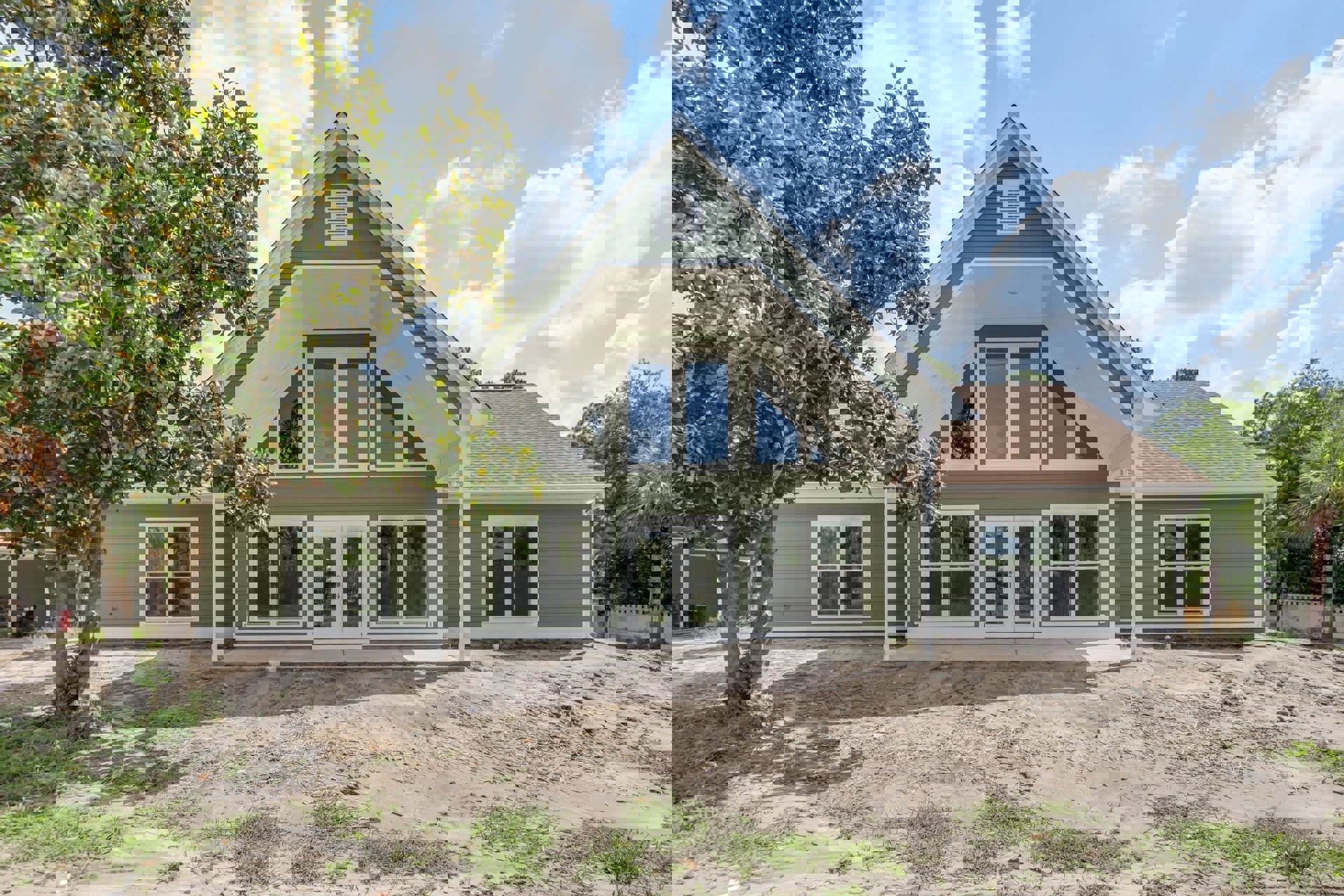 Two-story home with white siding, blue roof accents, white-framed windows, covered porch, and a leafy tree in the backyard under a partly cloudy blue sky