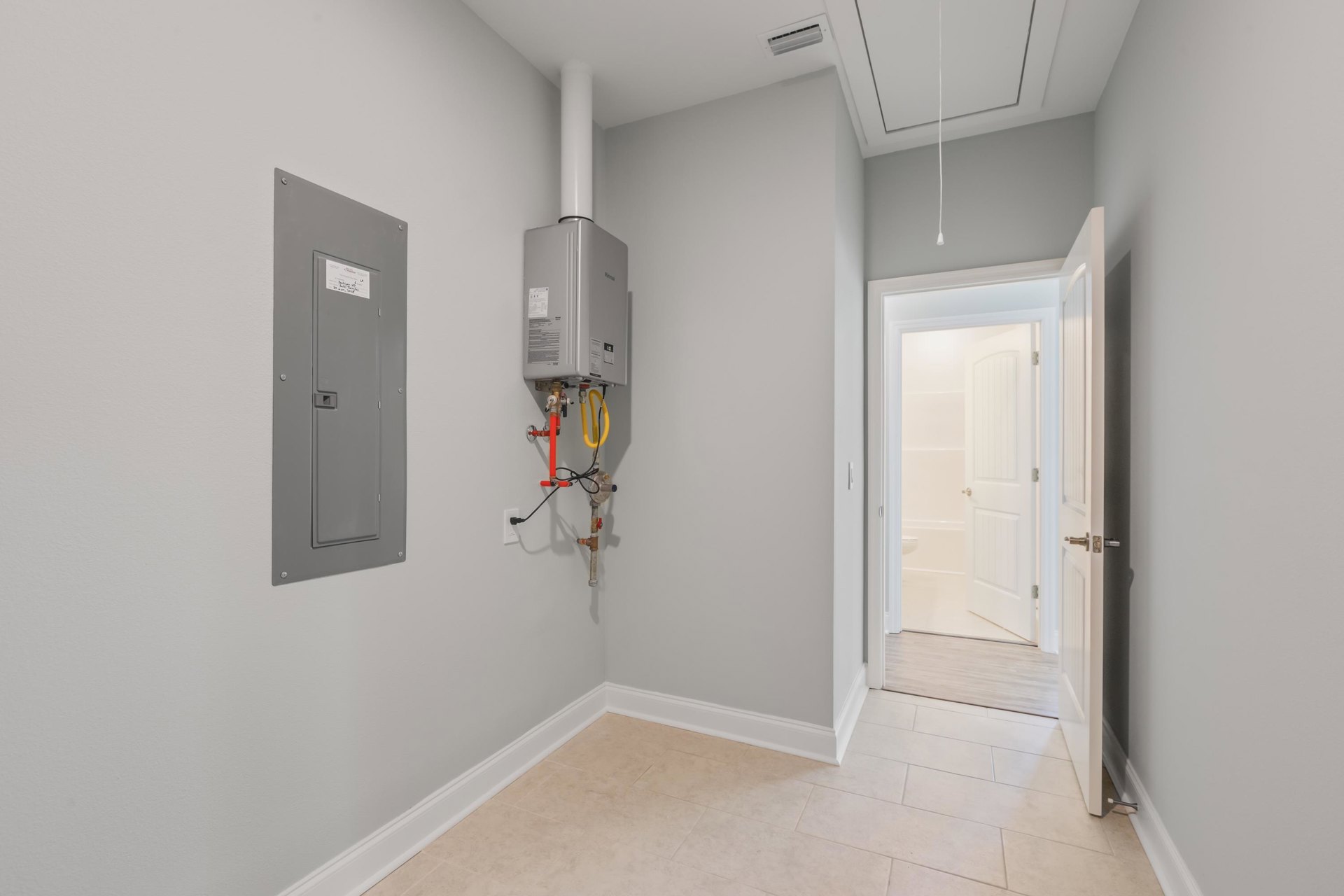 White tile floor and white walls in a bathroom with a white door open, revealing a toilet and bathtub; close-up of a refrigerator and grey door with a white sign also visible.