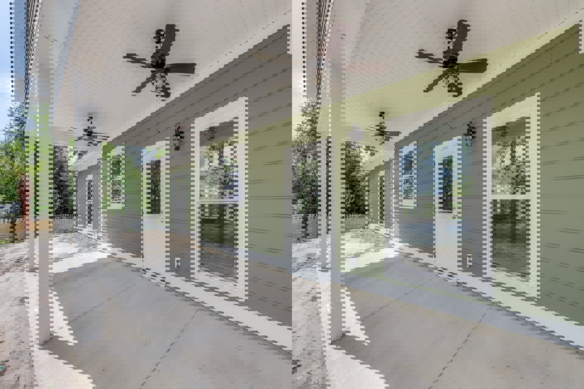 Green exterior house with white doors, ceiling fan with light on covered porch, black light fixture mounted on green wall, white-framed glass windows.