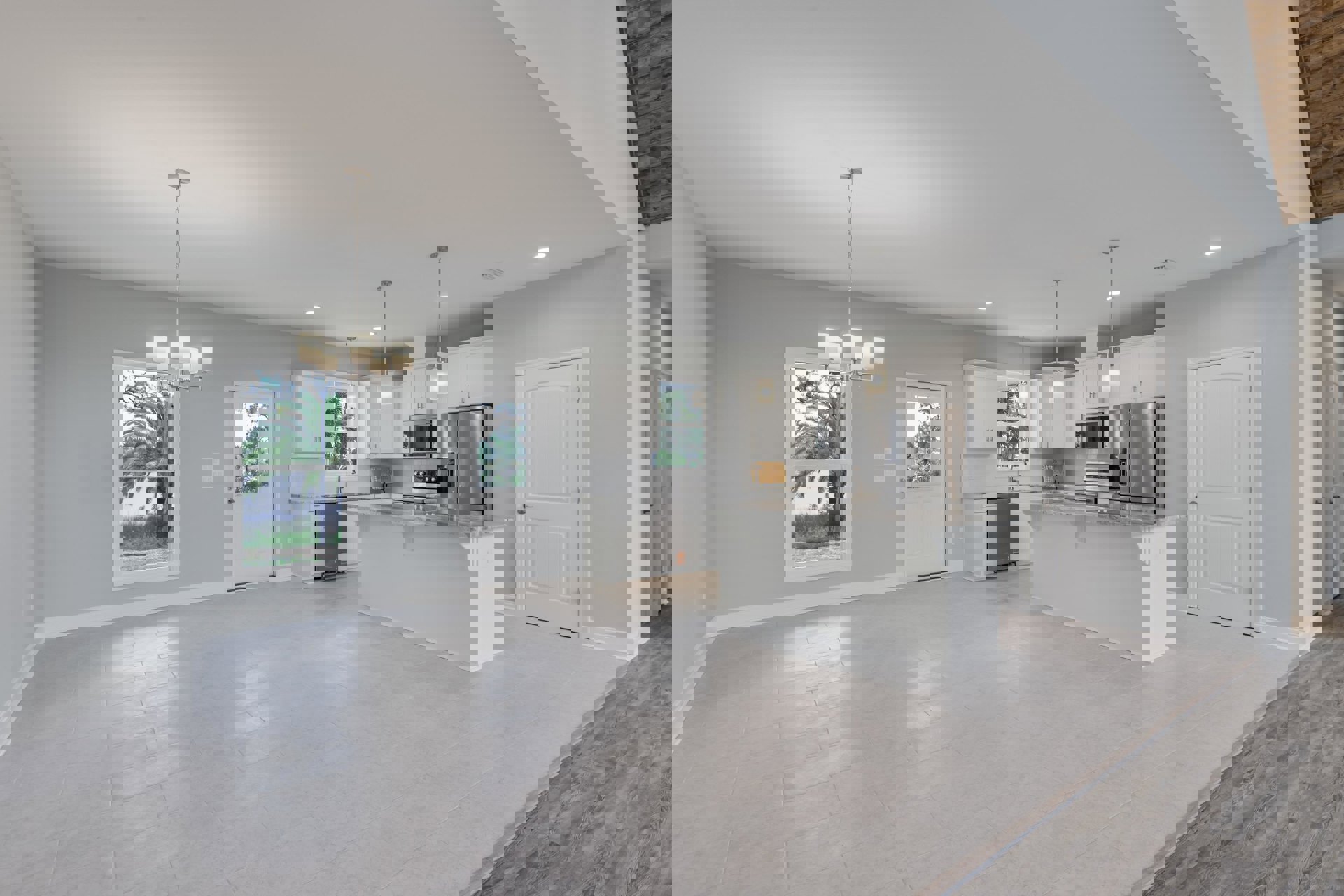 Open-concept kitchen and living room featuring white cabinetry, stainless steel refrigerator, glass-door microwave, white doors with silver handles, window with palm tree view