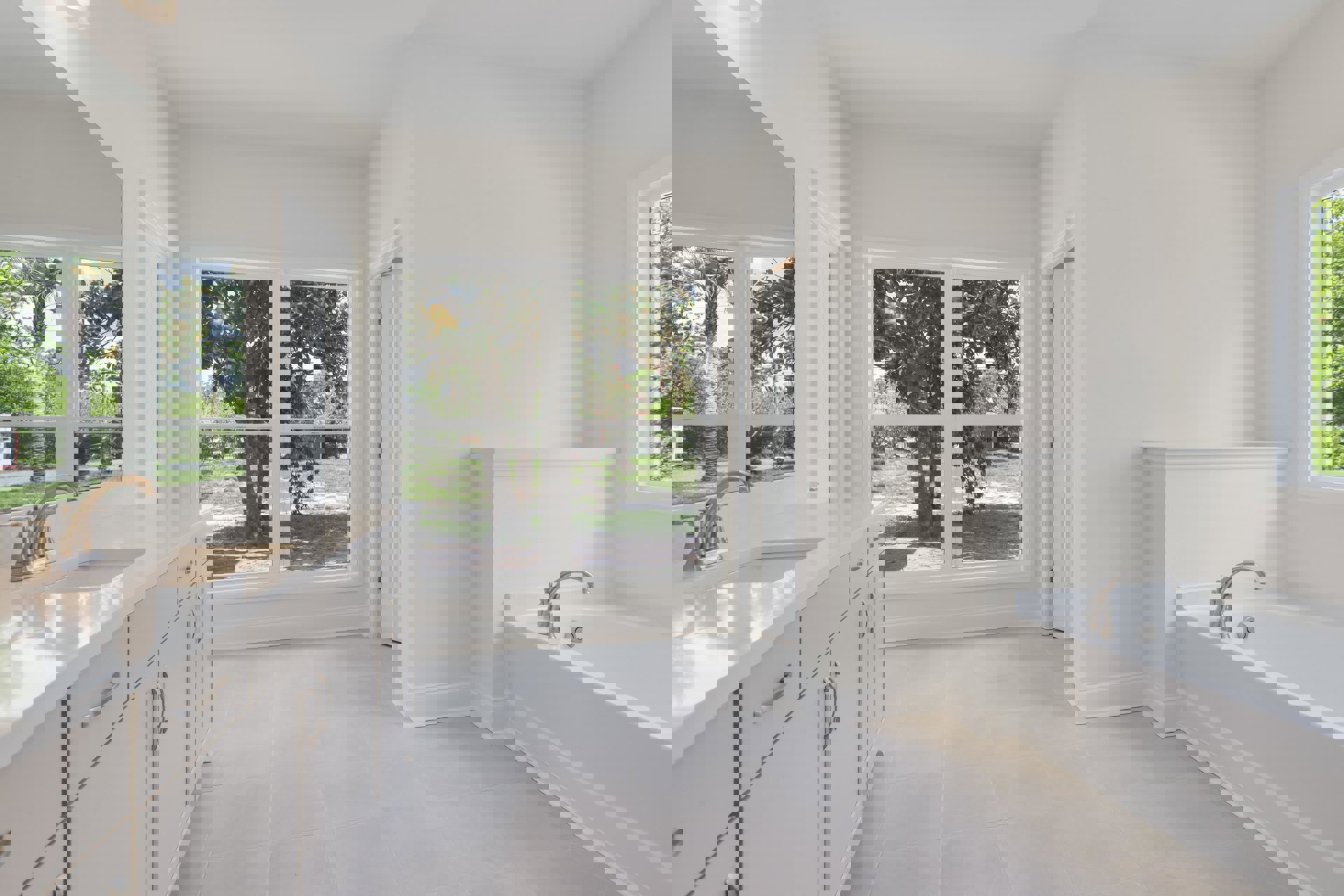 Bathroom with freestanding bathtub, modern sink on stone countertop, white tile walls, large window overlooking trees and grass