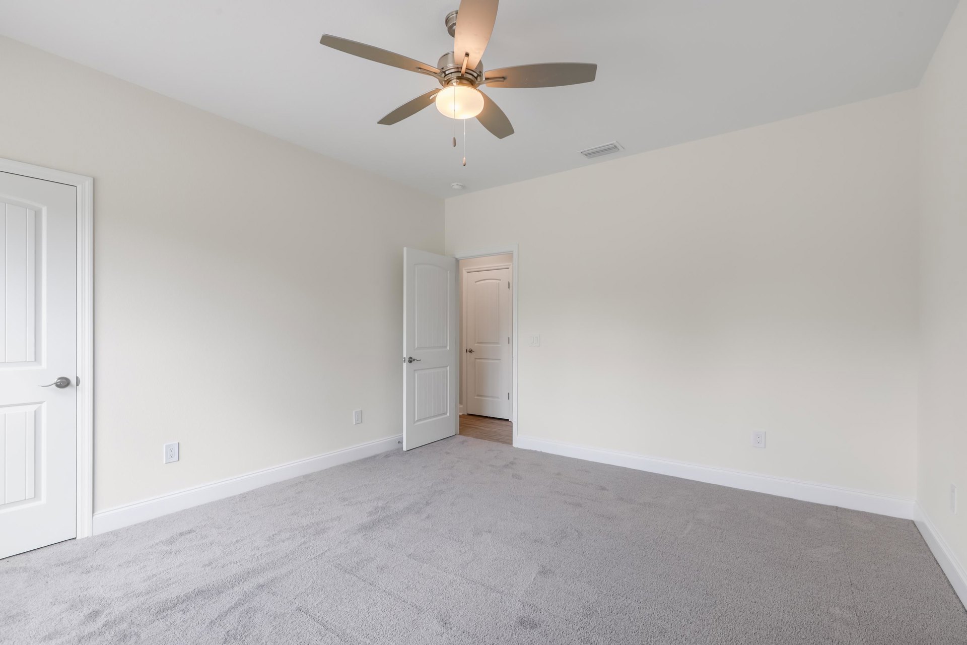 White paneled door with silver handle set in a white wall, wood flooring, and ceiling fan with light fixture overhead