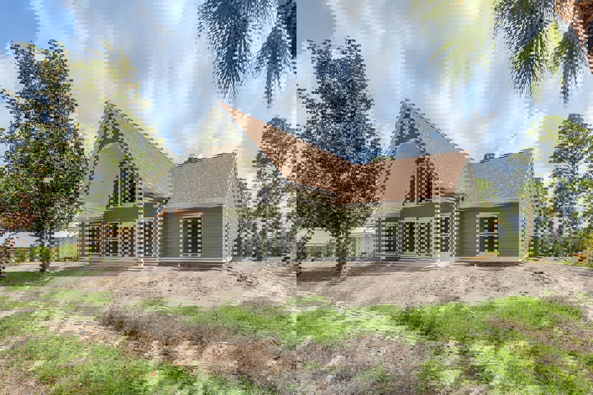 Two-story house with green roof, white-framed windows, spacious grassy yard, mature tree, and large gray HVAC unit near the porch.