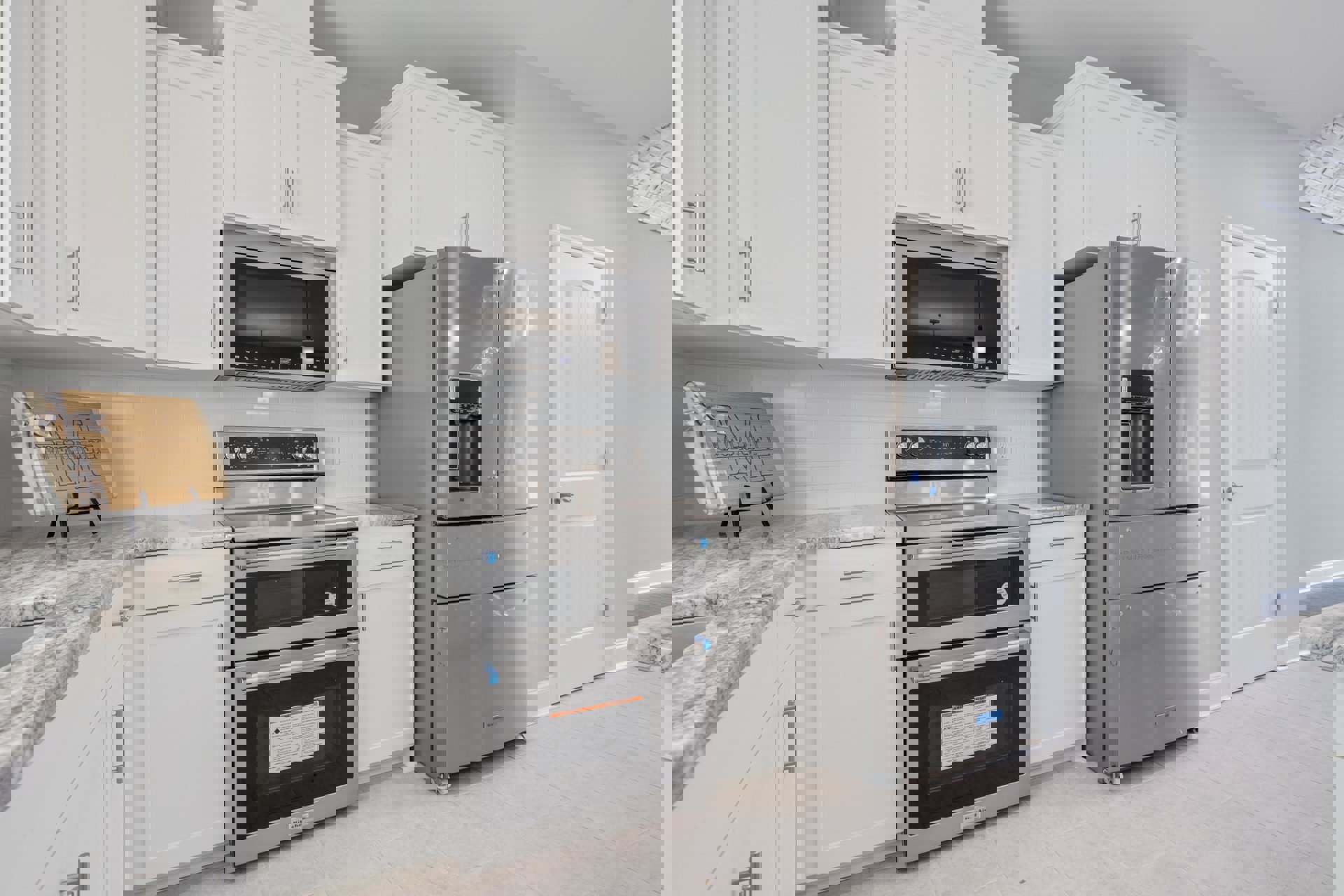 White kitchen cabinets, stainless steel appliances including oven and refrigerator, wooden cutting board with a bow on the countertop, microwave with interior light, open