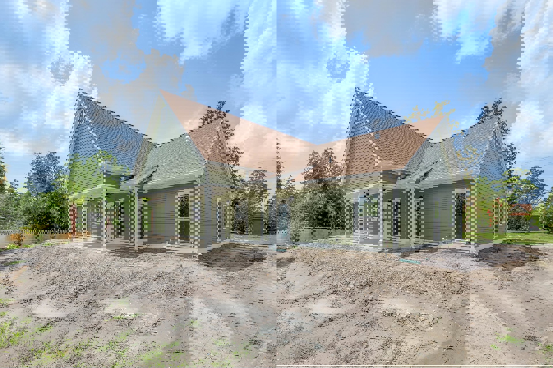 Green house with white trim surrounded by palm trees, dirt patch in front, white-framed window visible, construction materials and unfinished landscaping.