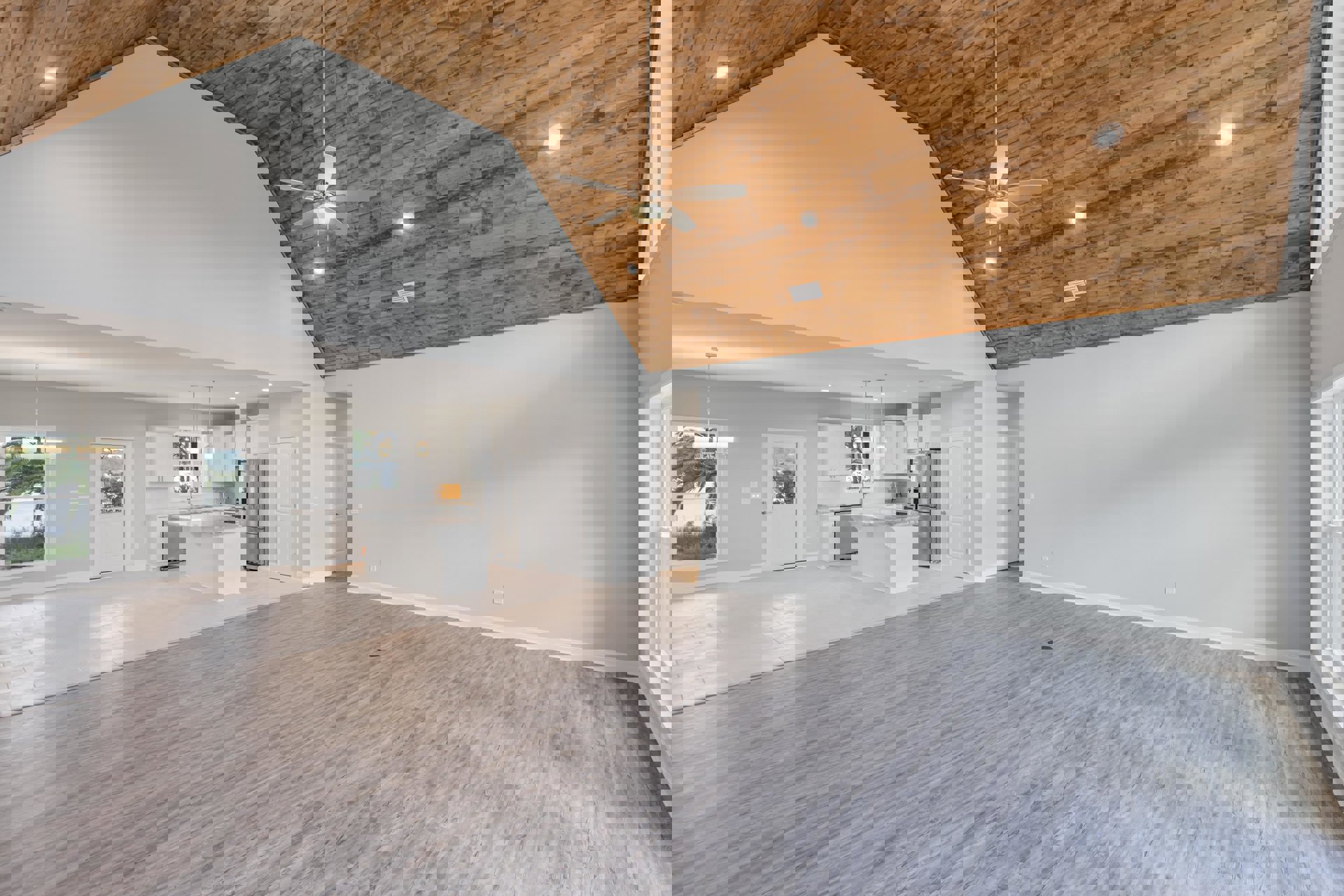 Open-concept living area with wood flooring, ceiling fan and light fixture, white kitchen featuring marble island, white door with window, and large window overlooking palm trees