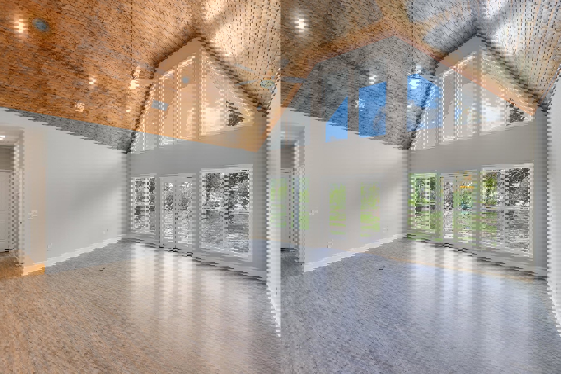 Spacious room with wood flooring, ceiling fan and light fixture, large windows, and white double doors with glass panes and silver handles