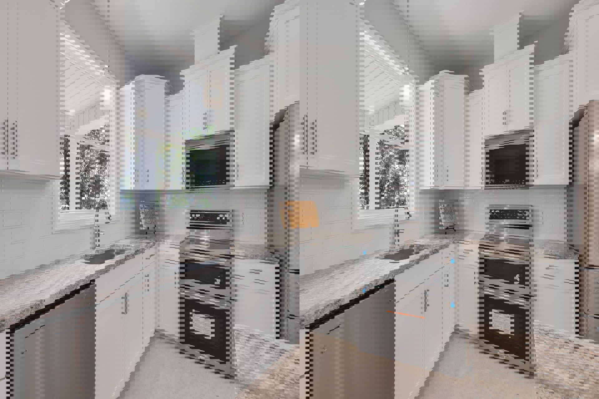 White kitchen with marble countertops, stainless steel oven, built-in microwave, wood cutting board, and upper and lower cabinetry