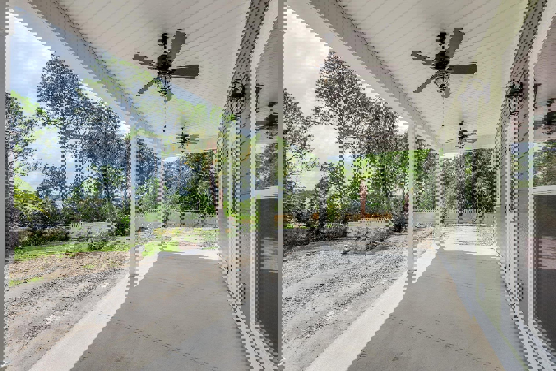 Covered porch with wood ceiling, ceiling fan with light, white railing, and leafy tree in background