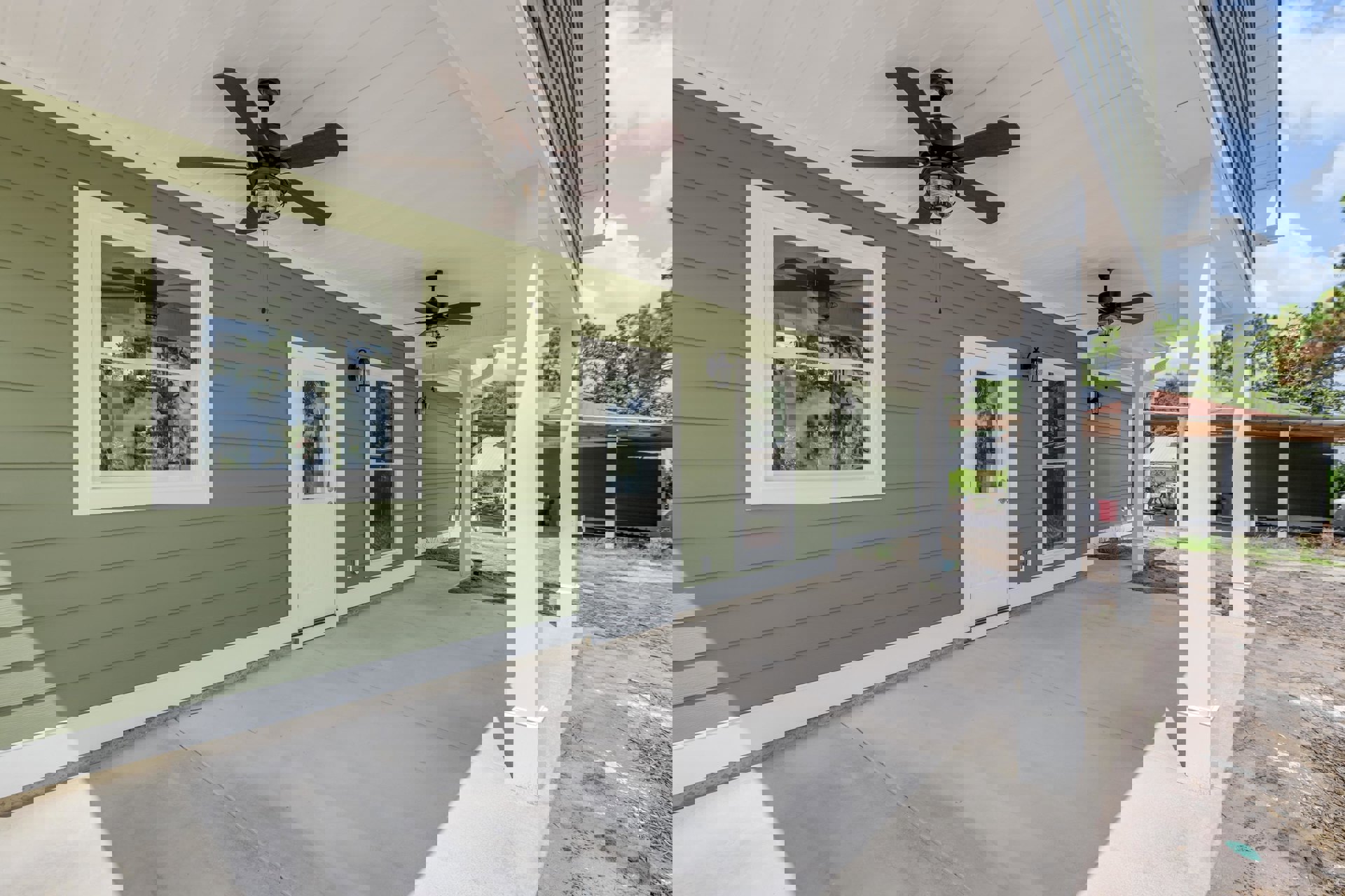 Green exterior house with white columns, covered porch, ceiling fan with light, white door with window, multiple windows, and fenced yard.